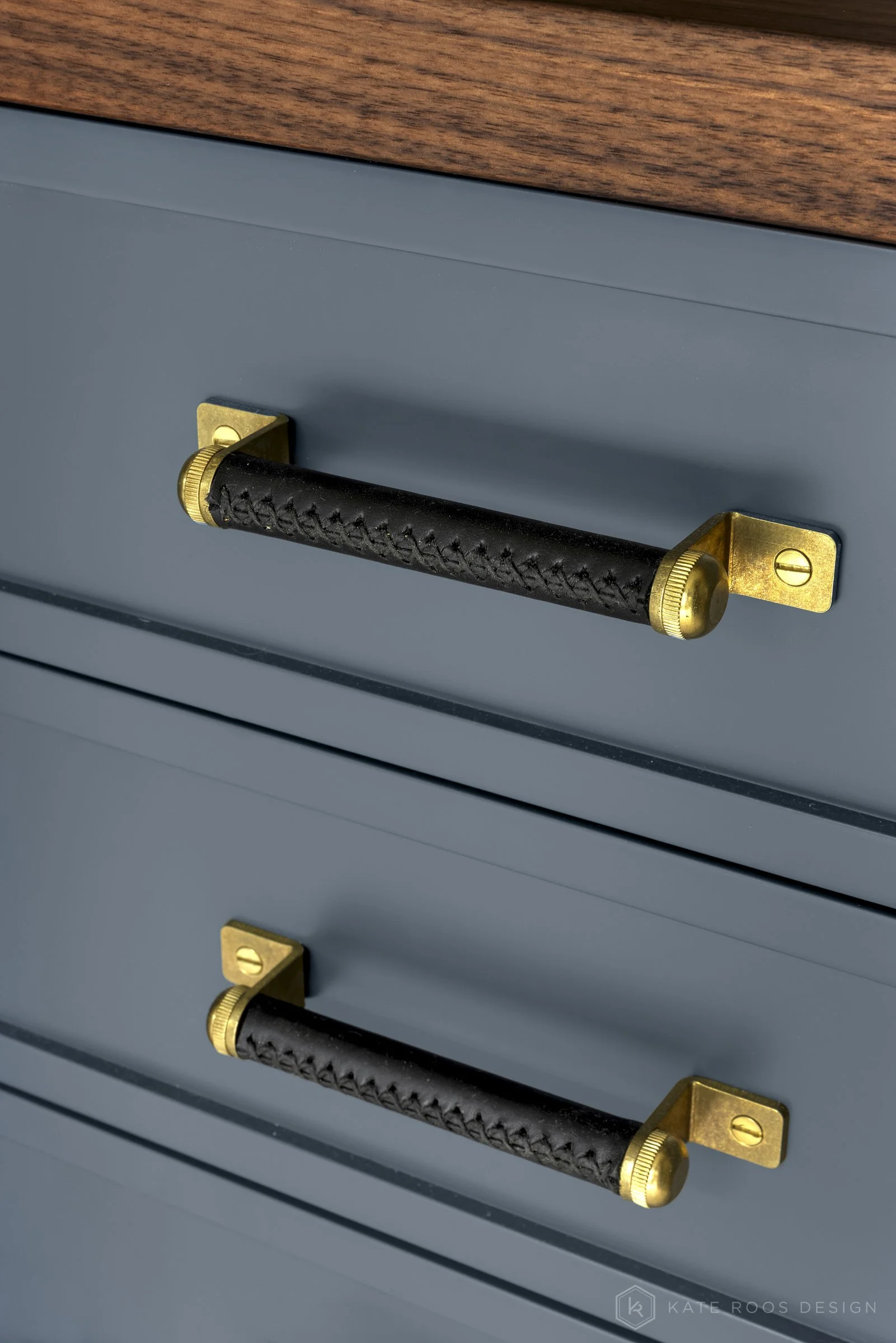 This image showcases a beautifully designed home office that balances function, comfort, and style. The space features a built-in desk with rich wood countertops and deep navy cabinetry accented by brass hardware, creating a sophisticated yet invitin