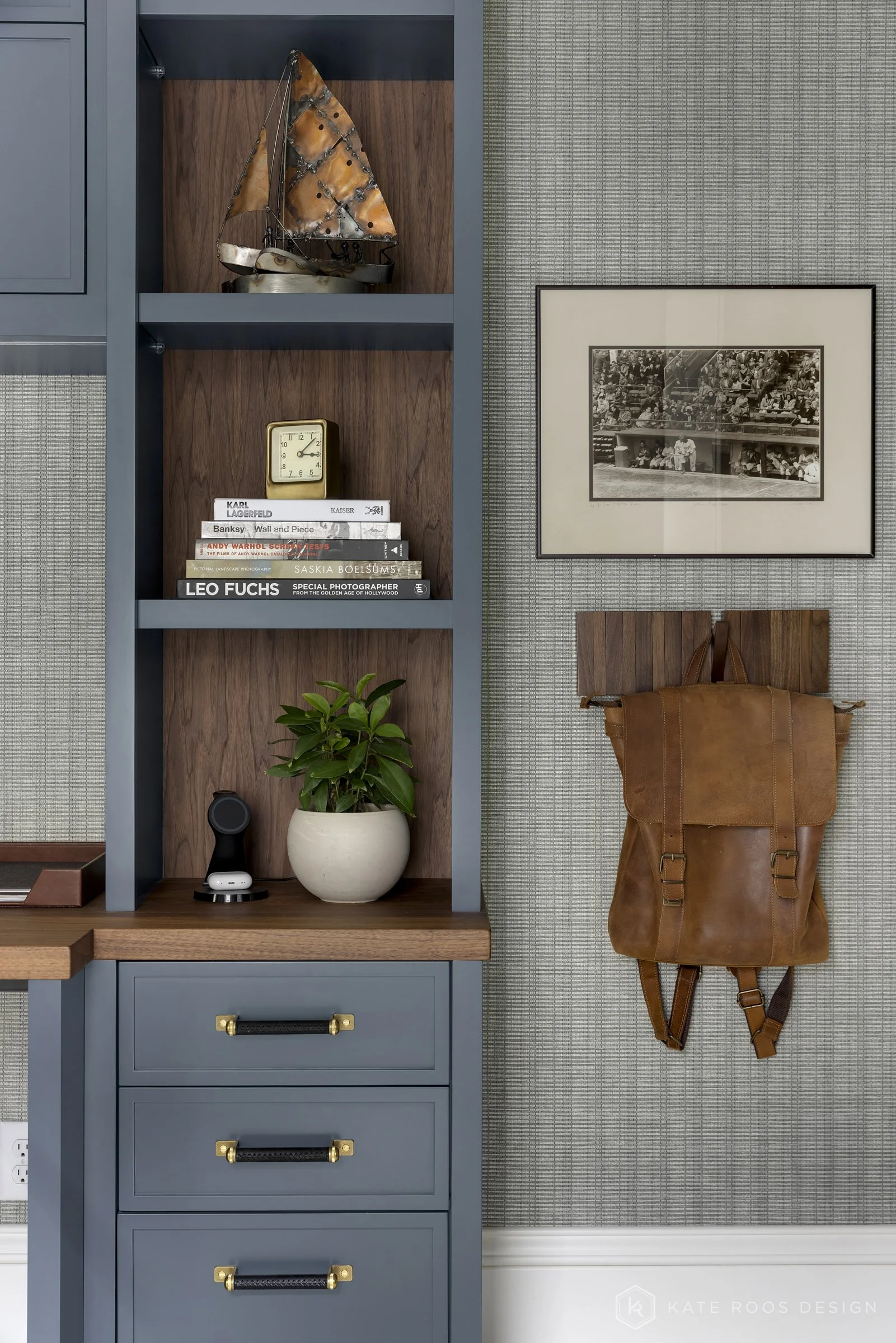 This image showcases a beautifully designed home office that balances function, comfort, and style. The space features a built-in desk with rich wood countertops and deep navy cabinetry accented by brass hardware, creating a sophisticated yet invitin