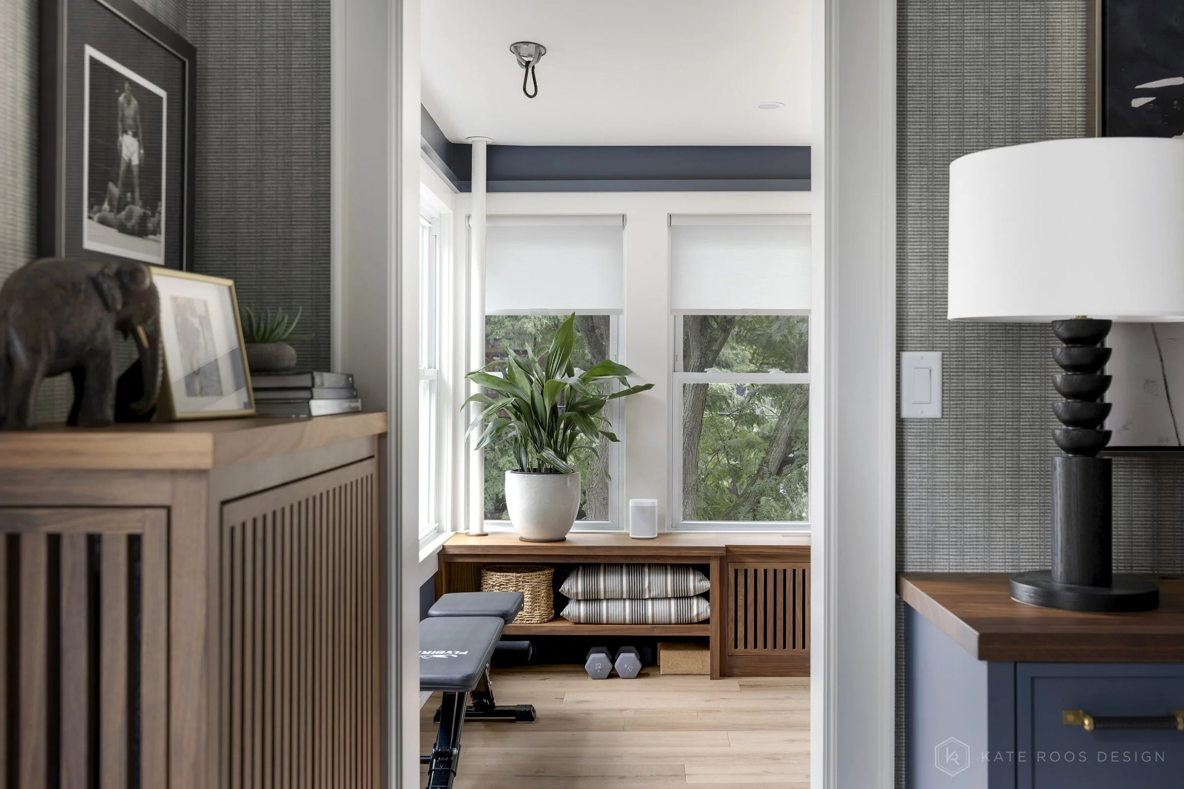 This image showcases a beautifully designed home office that balances function, comfort, and style. The space features a built-in desk with rich wood countertops and deep navy cabinetry accented by brass hardware, creating a sophisticated yet invitin