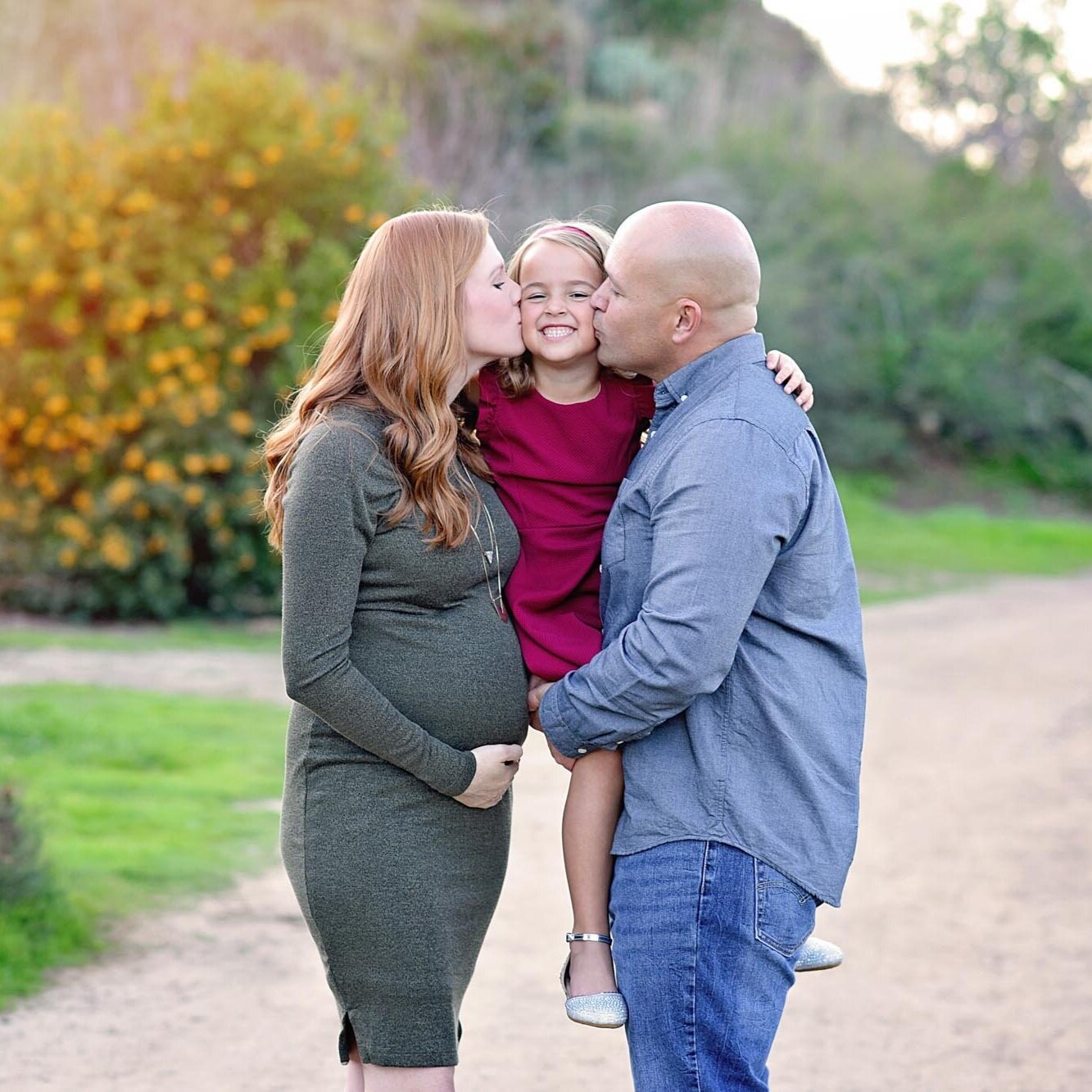 Pregnant mother and father kissing daughter in Orange County CA