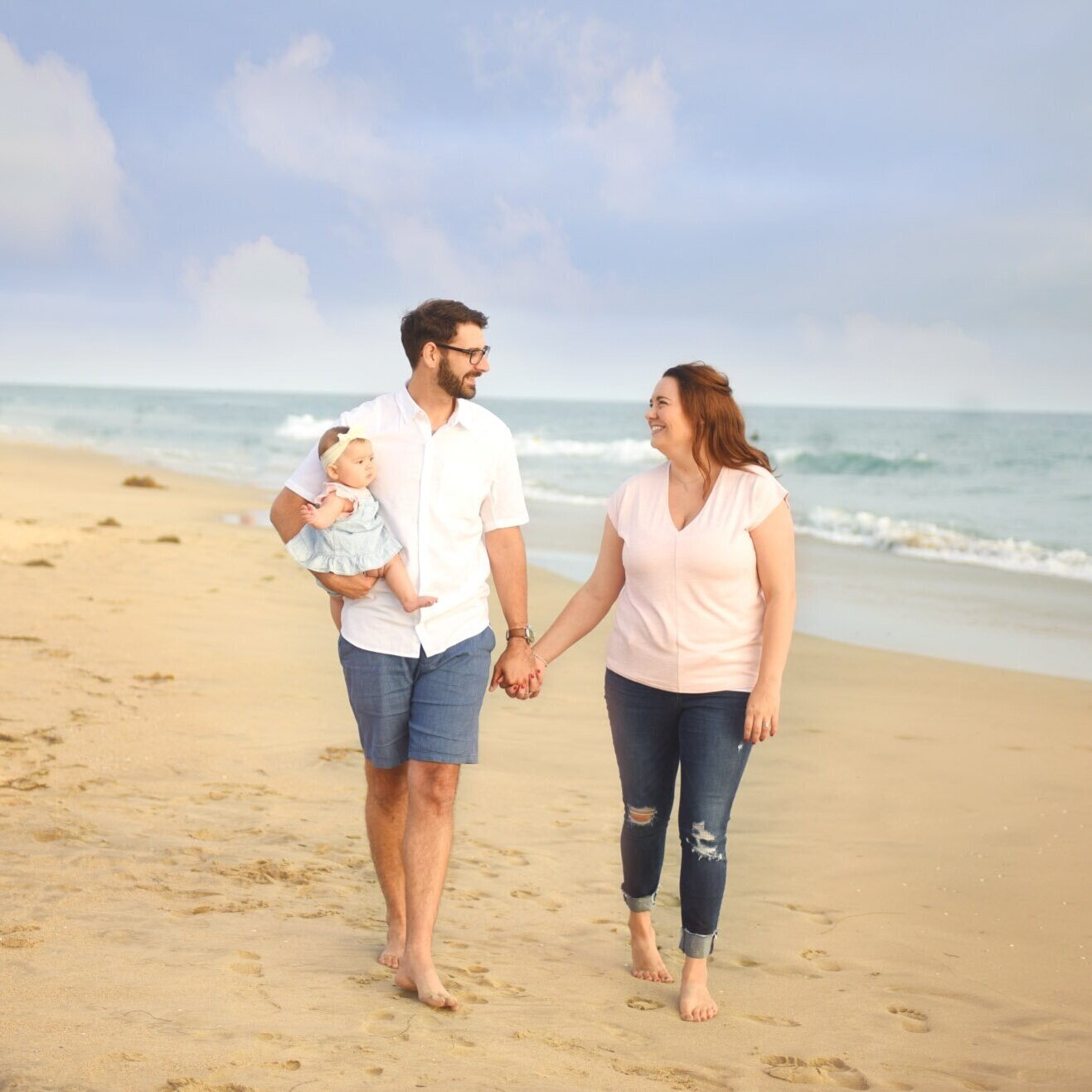 Couple holding hands with baby daughter in Huntington Beach CA