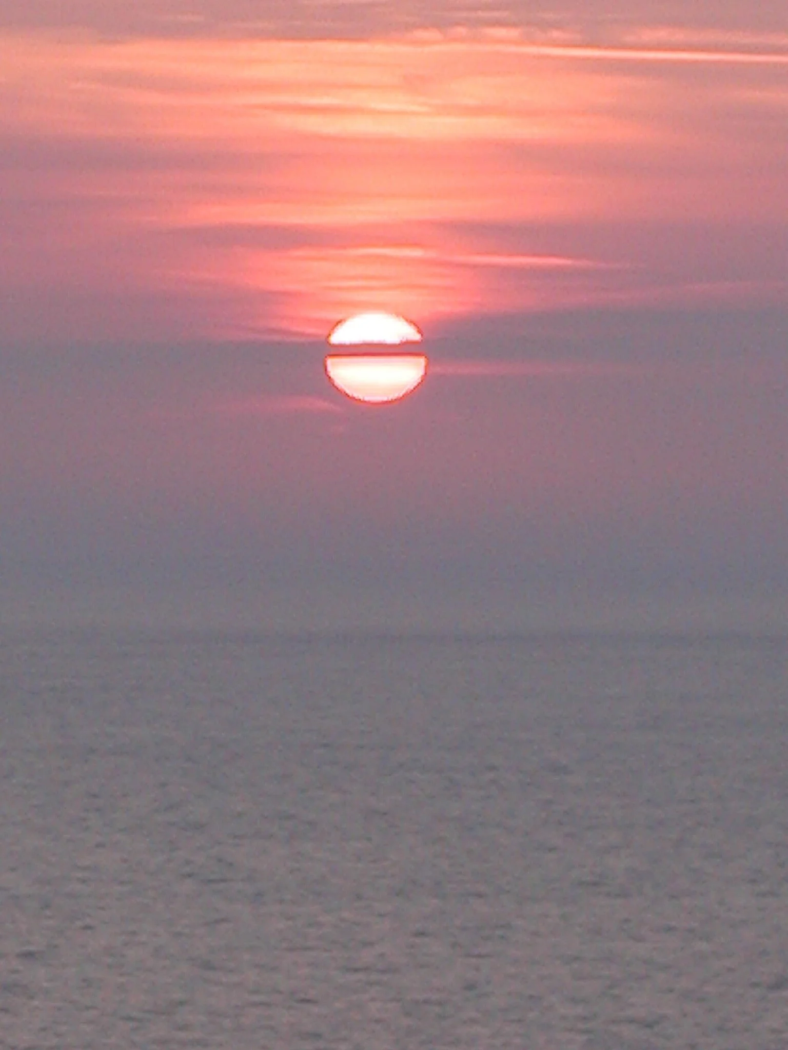 Sunset over the ocean with pink and orange clouds.