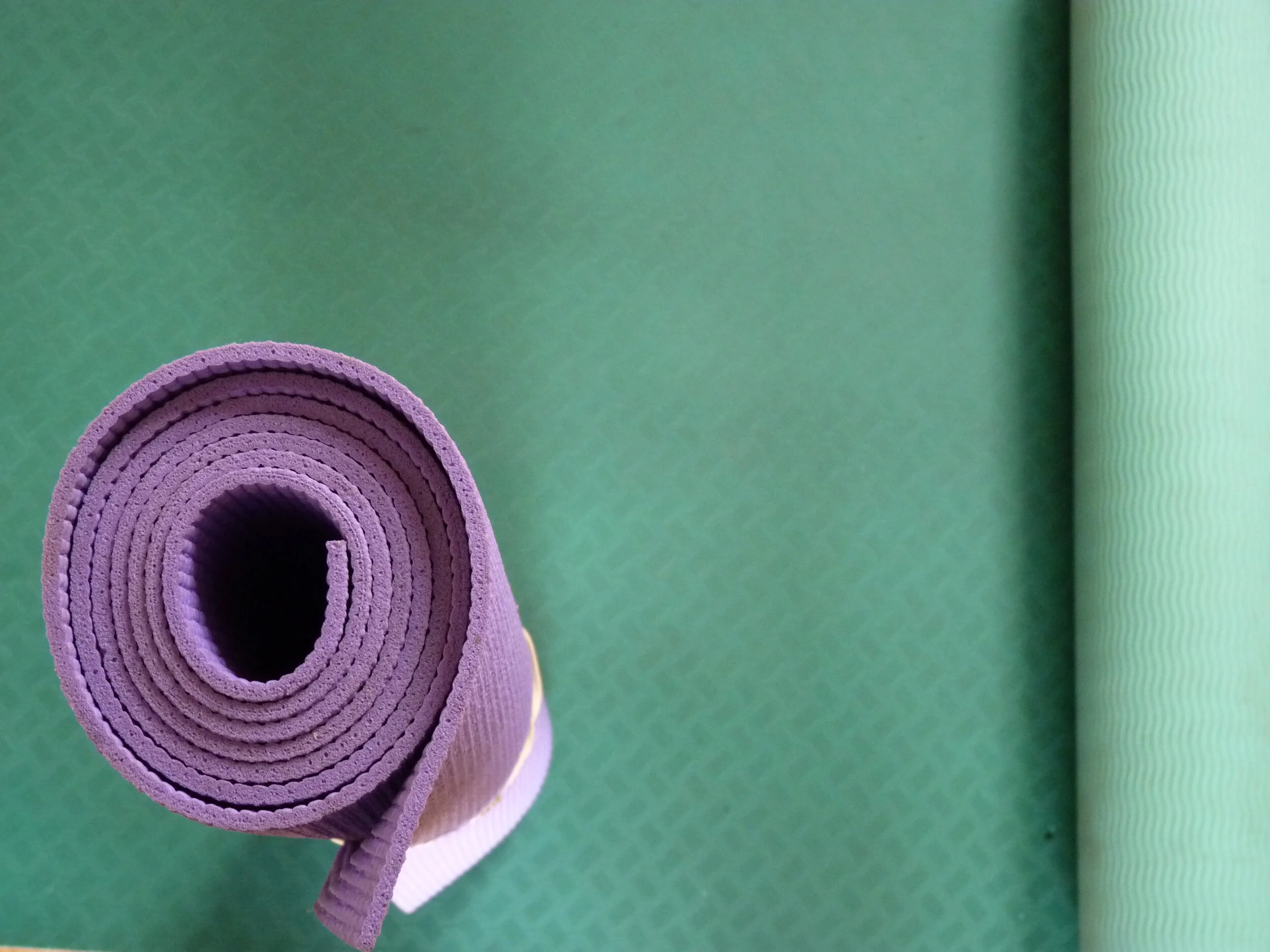 Rolled purple yoga mat on green yoga mat surface