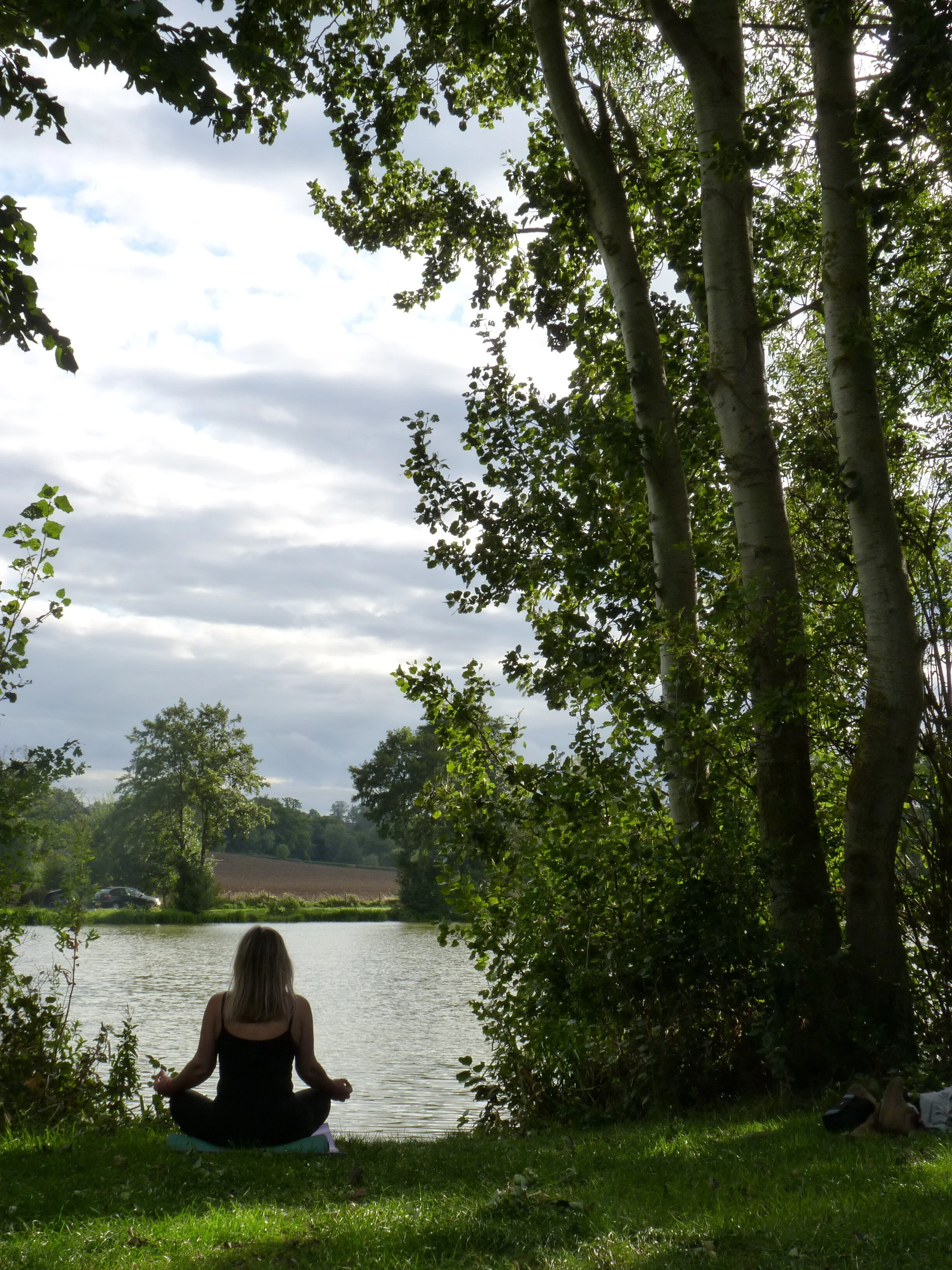 Person meditating by a lake surrounded by trees