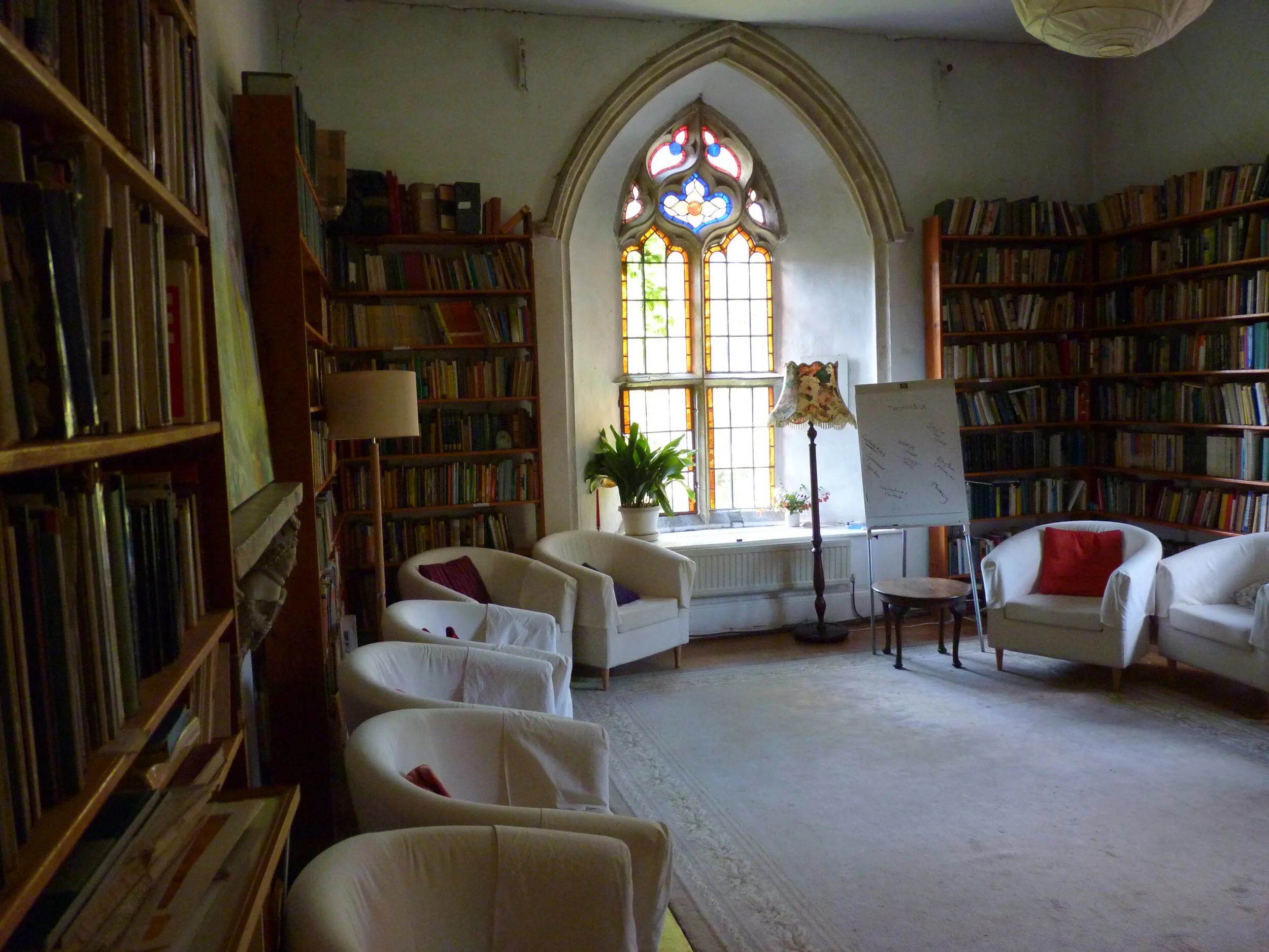 Room with bookshelves, arch window, white chairs, a lamp, and a whiteboard.
