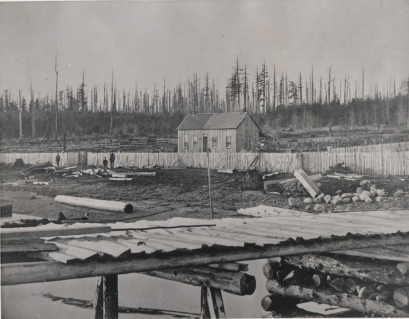  First wharf and house of Timothy and Flora (Woodcock) Mangan. They homesteaded around 1871 on the south shore of Guemes Island. Three people are in photo at left. Note evidence of forest fire. (Fire swept through the island in 1885) The Mangans also