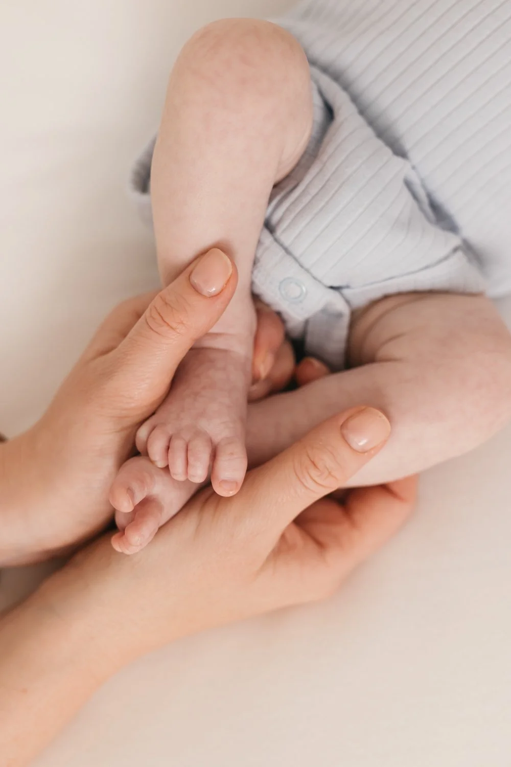 Close-up of an adult holding a newborn baby in their hands, focusing on the baby's tiny feet and hands.