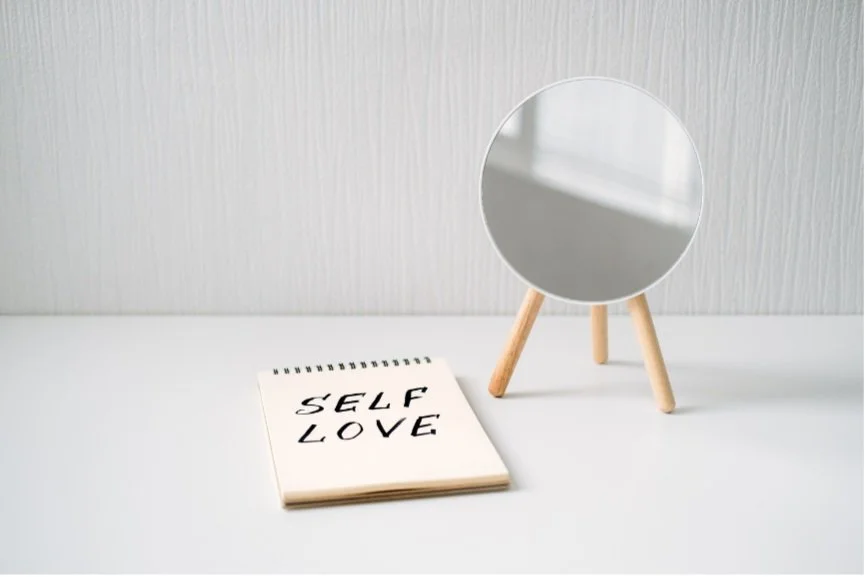 Self Love written on a notebook next to a small mirror
