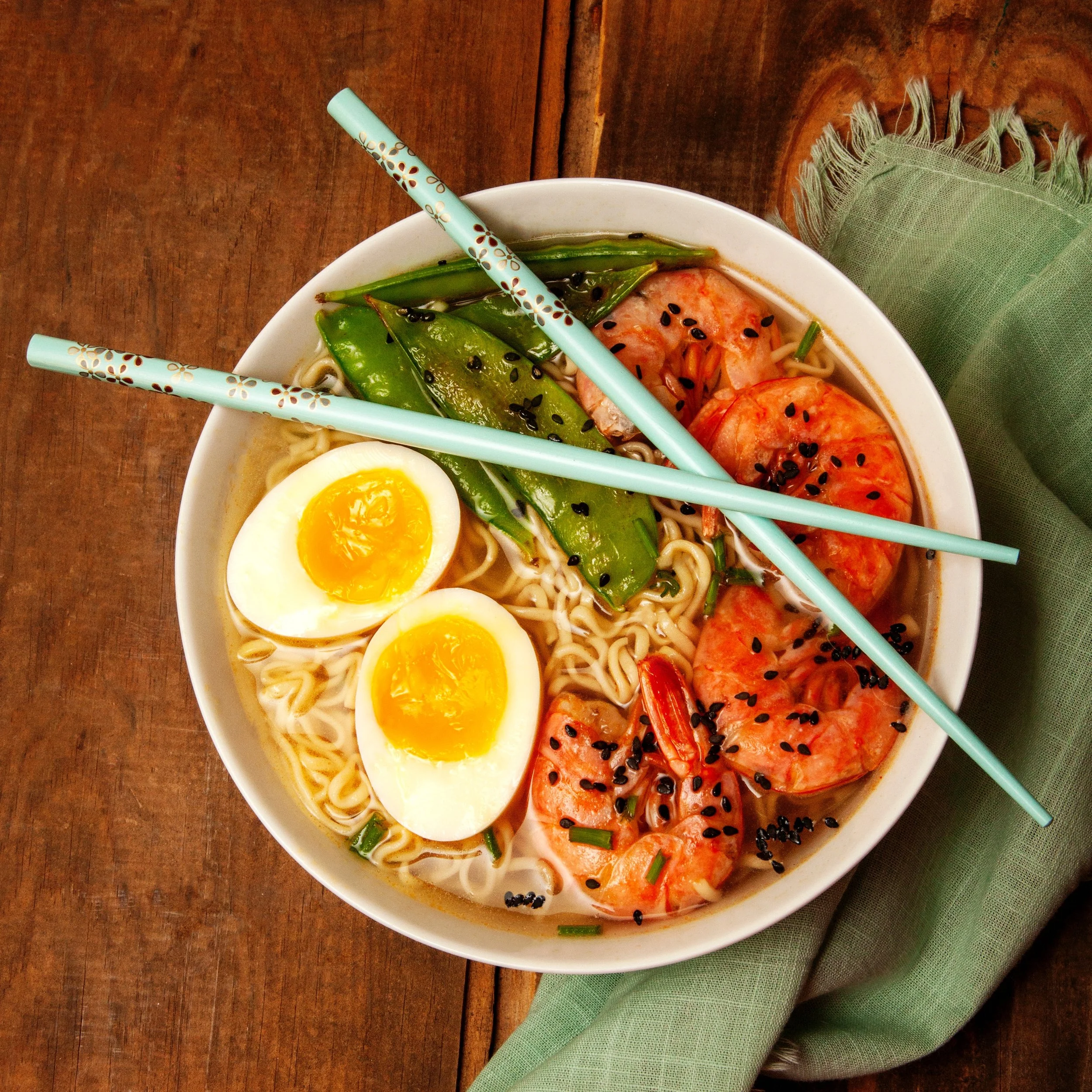 ramen with boiled egg, shrimp, and snow peas with blue chopsticks