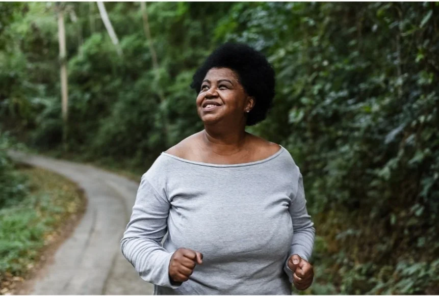 Black woman in a grey long-sleeve shirt walking on a tree-lined path