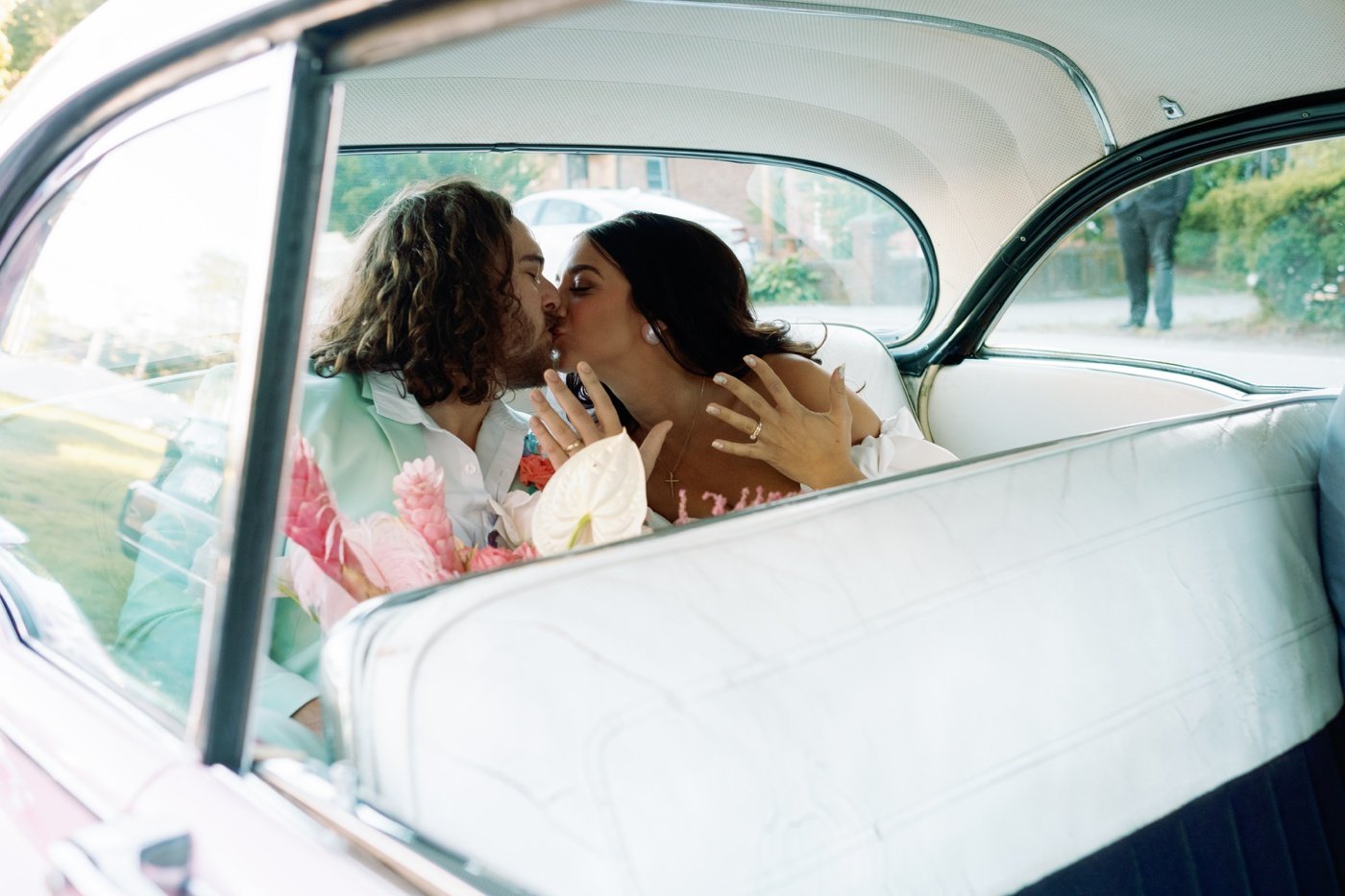 Bride and groom inside a pink vintage Cadillac after their wedding ceremony