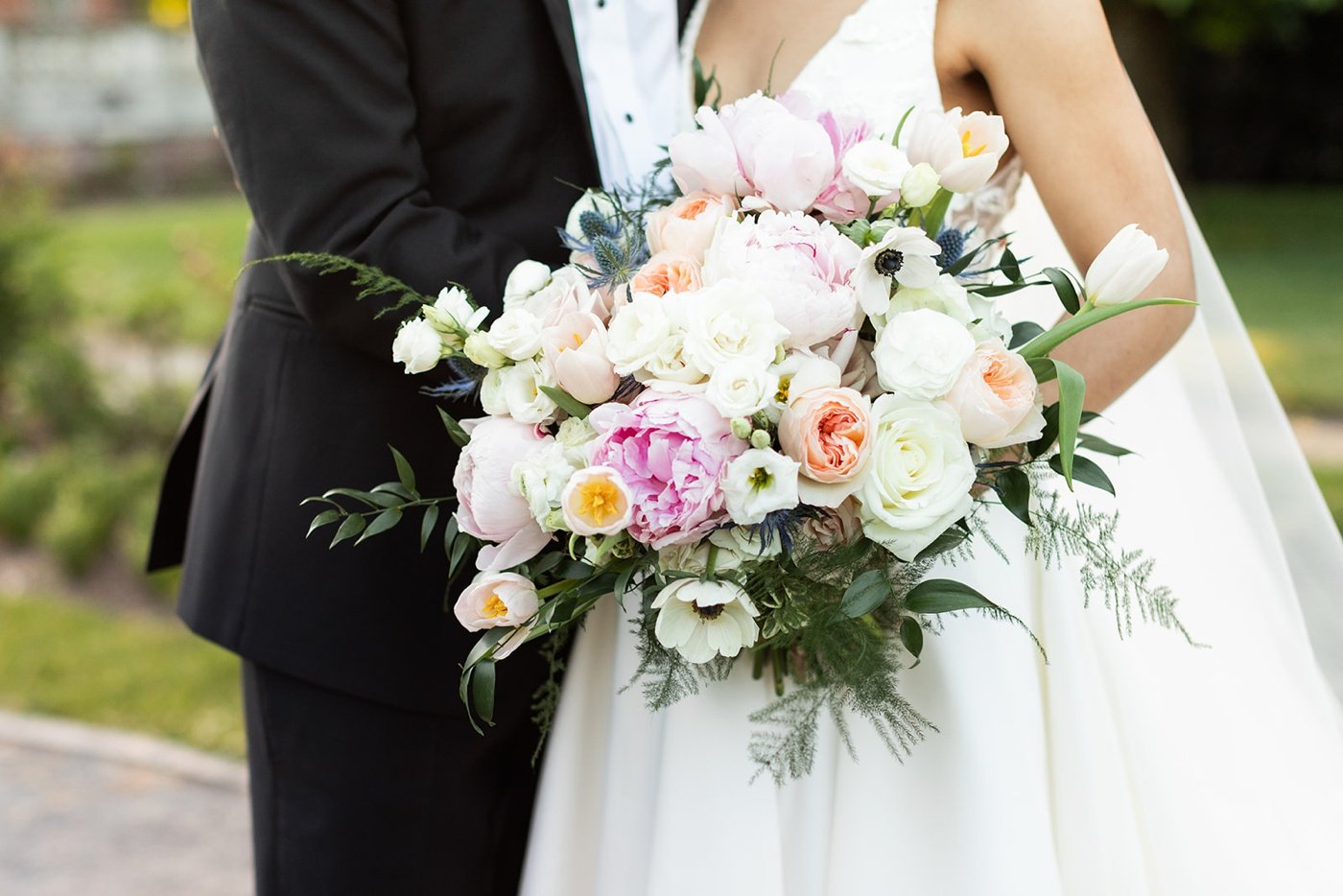 Bride holding a garden-inspired wedding bouquet filled with pink peonies, peach garden roses, and anemones by Sayles Livingston Design
