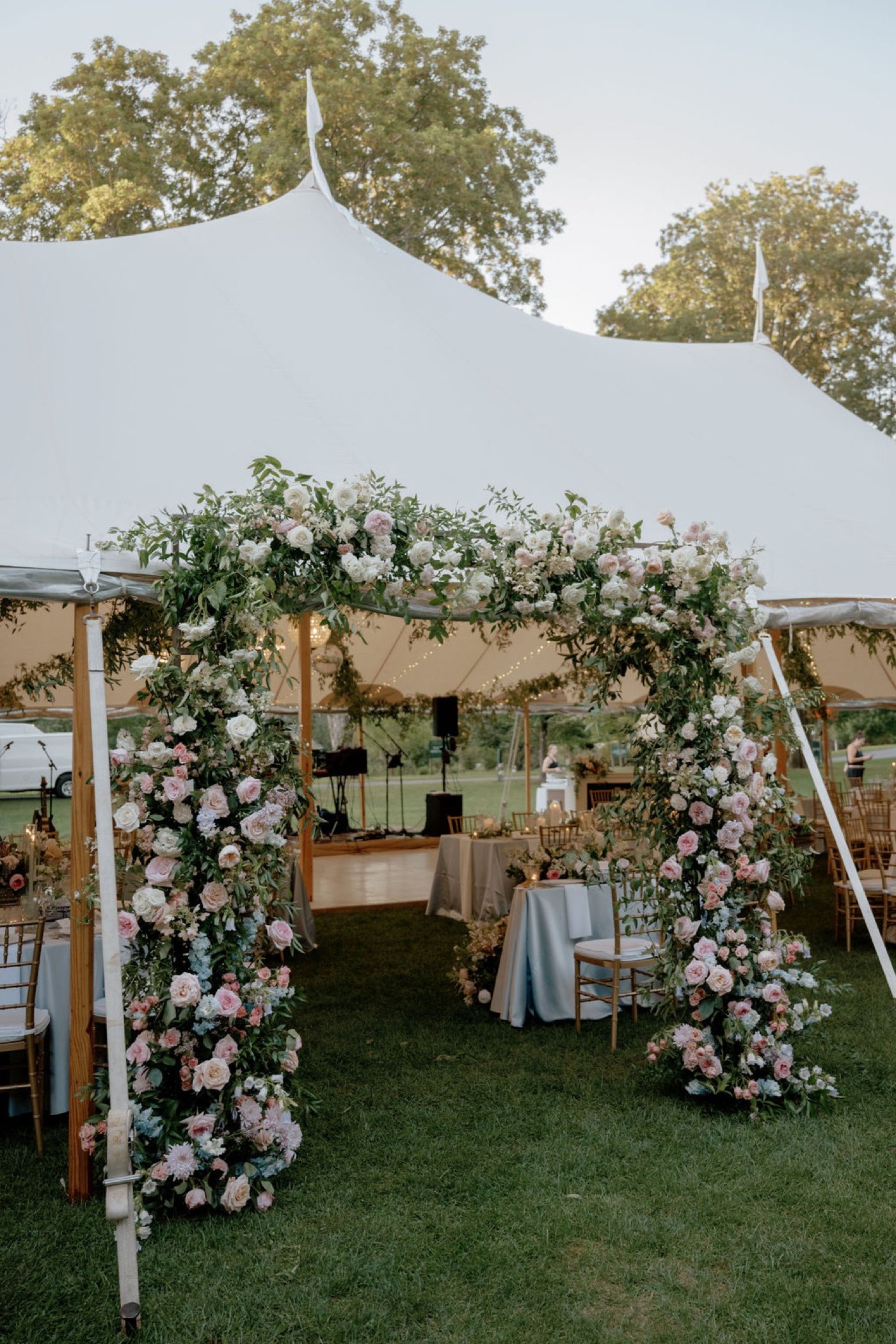 Floral archway with pink and white roses at the entrance to a tented wedding reception