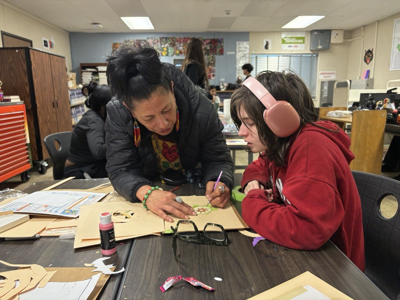 Teaching Artist Lilia Ramirez carefully cuts a stencil alongside a Jack London student. 