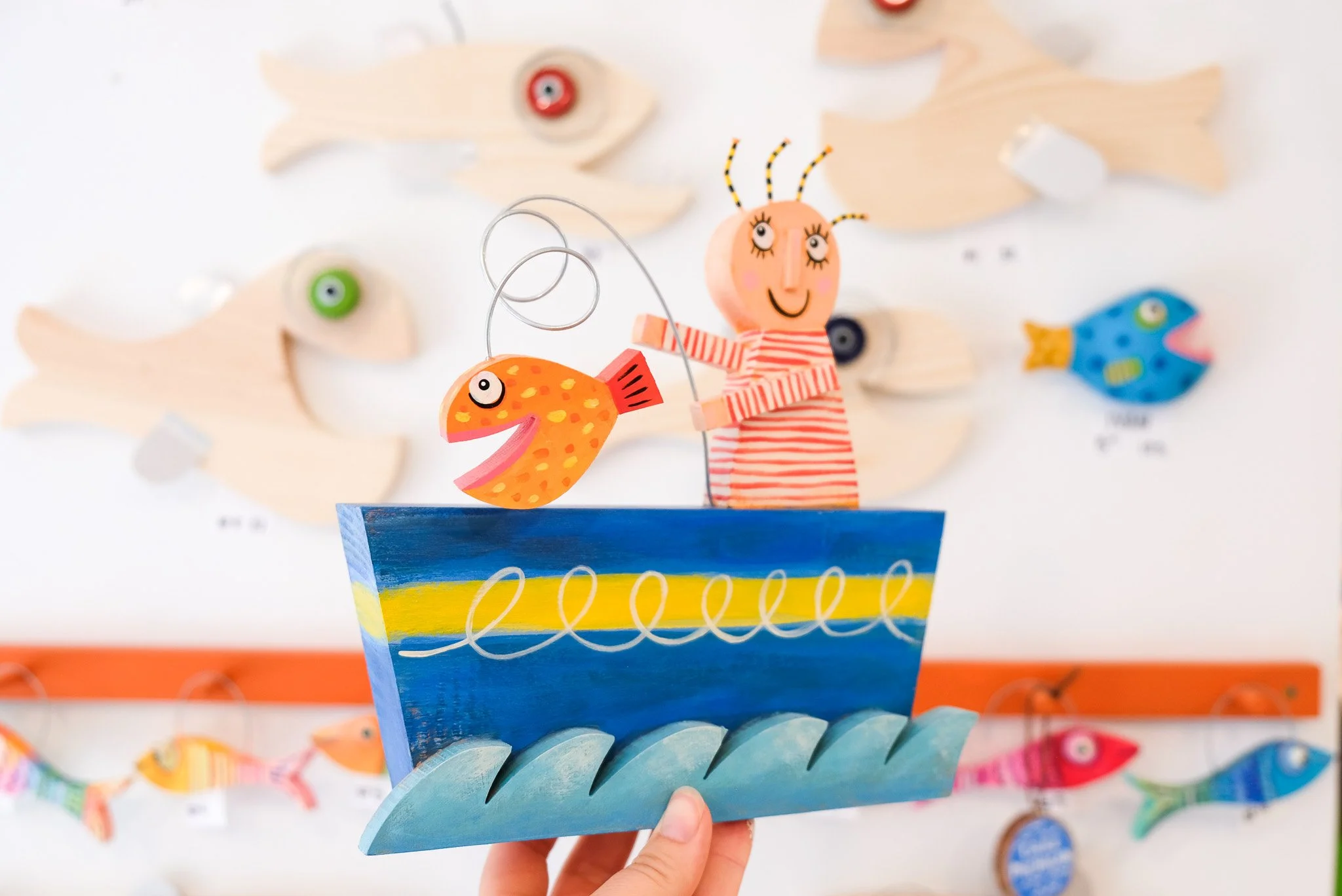 A colorful wooden boat with a smiling person holding a fishing pole with a fish on it, surrounded by fish and sea-themed decorations on the wall.