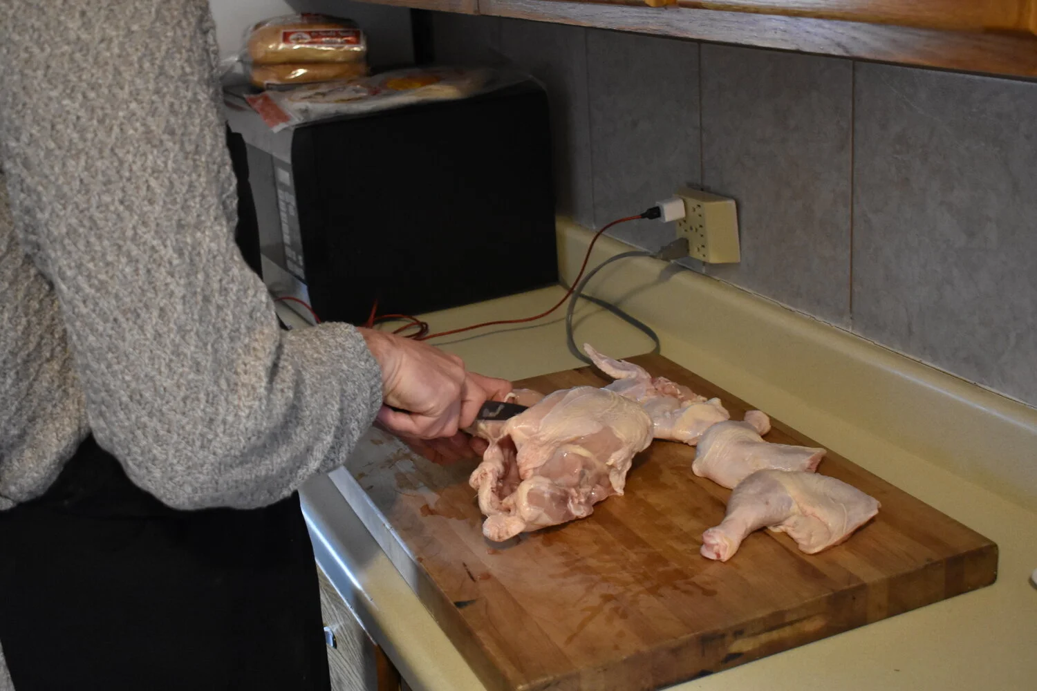 Person cutting raw chicken on a wooden cutting board in a kitchen.