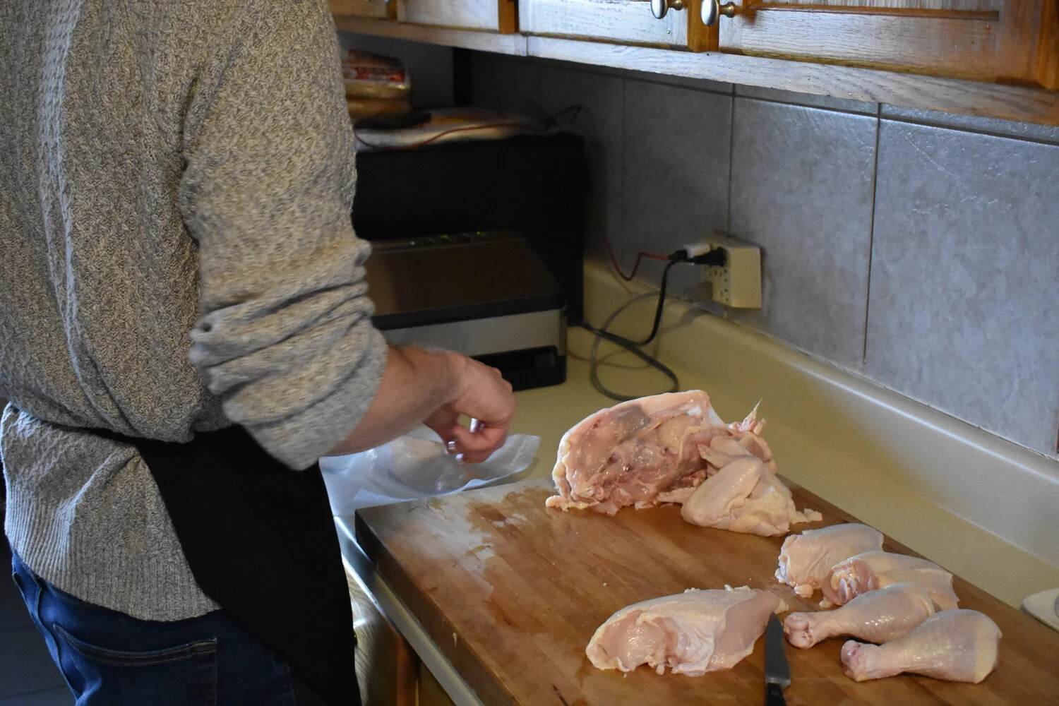 Person preparing raw chicken pieces on a wooden cutting board in a kitchen.