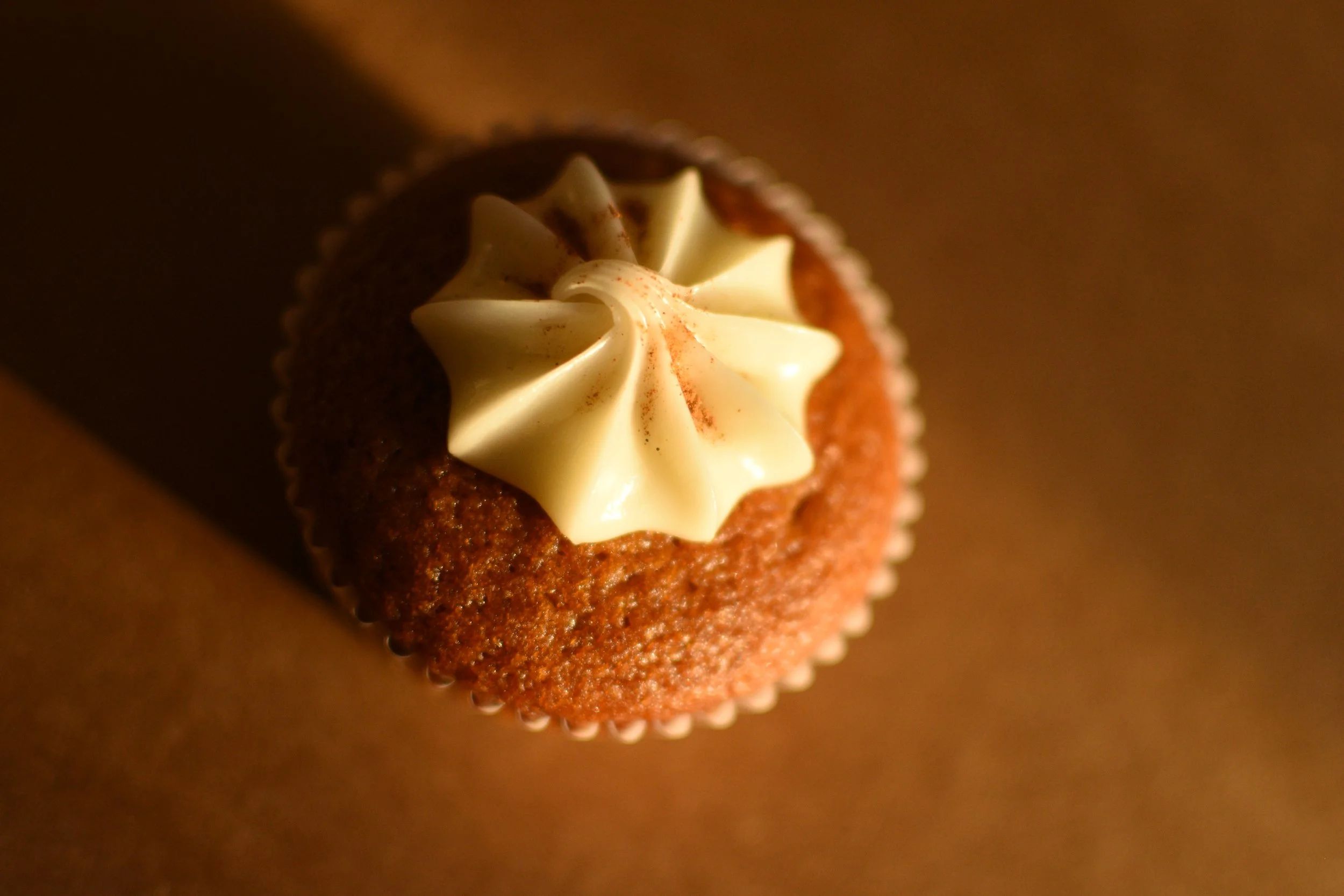 Close-up of a cupcake with white frosting topped with a light dusting of red powder, in a white paper liner.