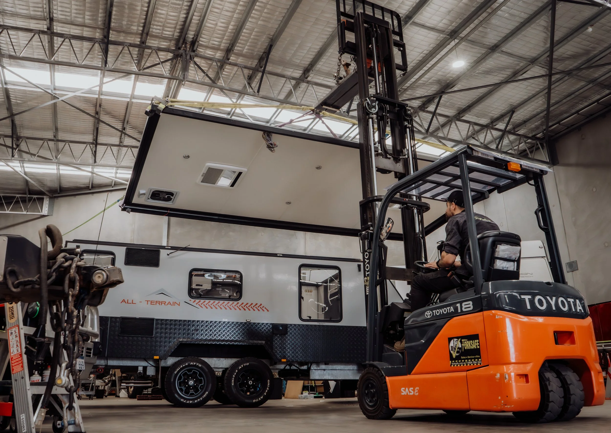 A man operating a forklift inside a large industrial space, lifting a ceiling panel for installation or maintenance.