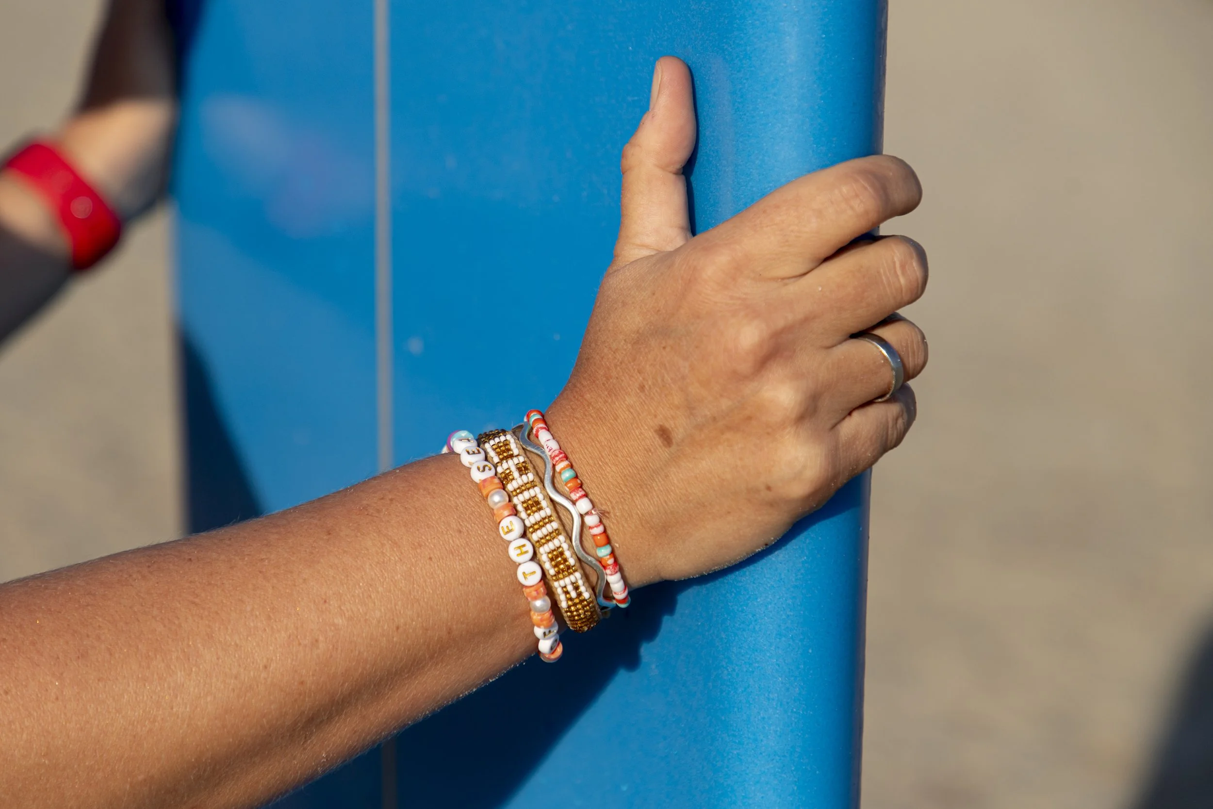 Michi holds the sides of her surfboard - bracelets read 'sisters of the sea' and 'choice'