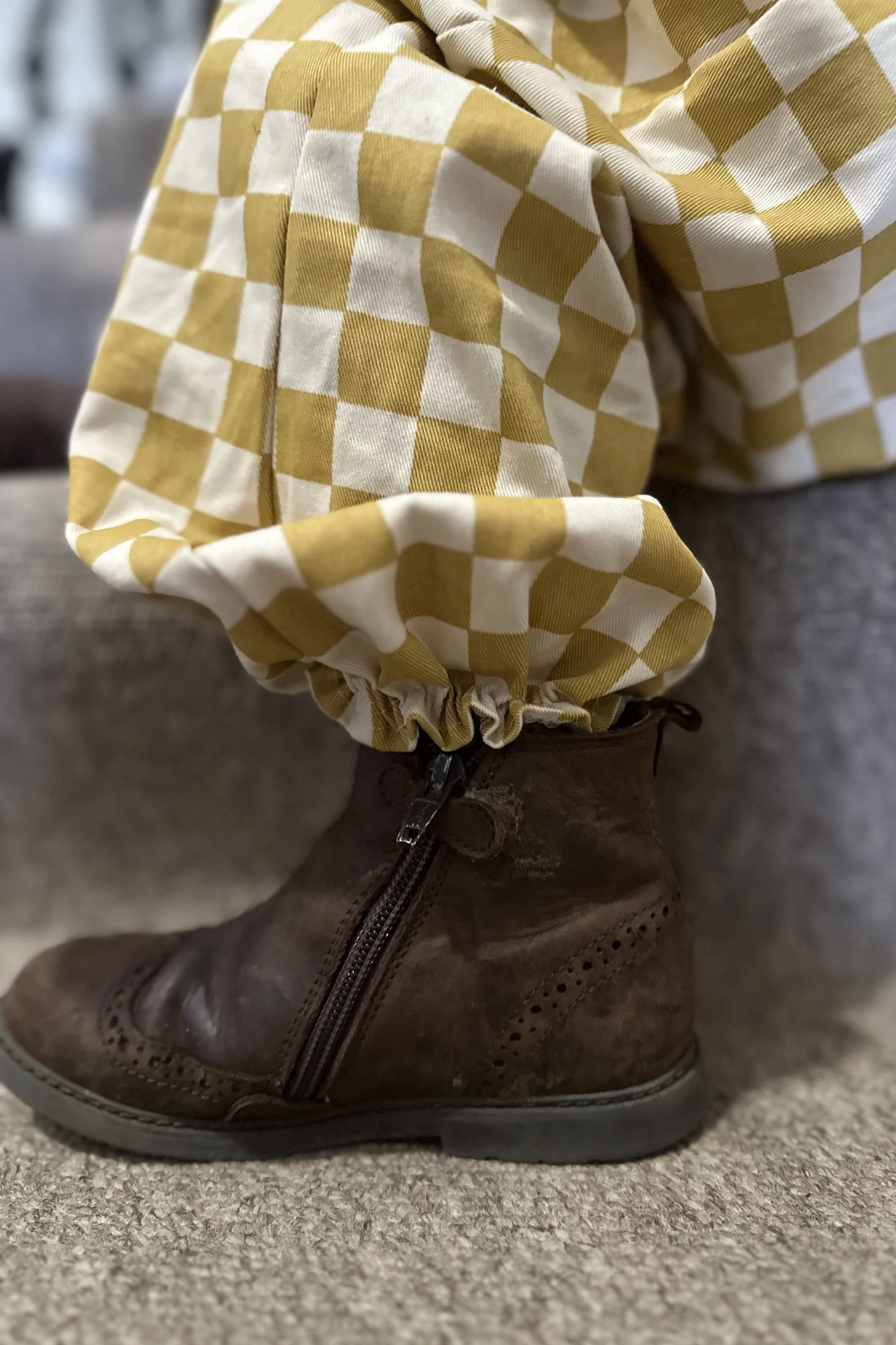 close up at ankle of child wearing organic cotton checkerboard mustard pullover dungarees, with brown boots, highlighting elastic hem
