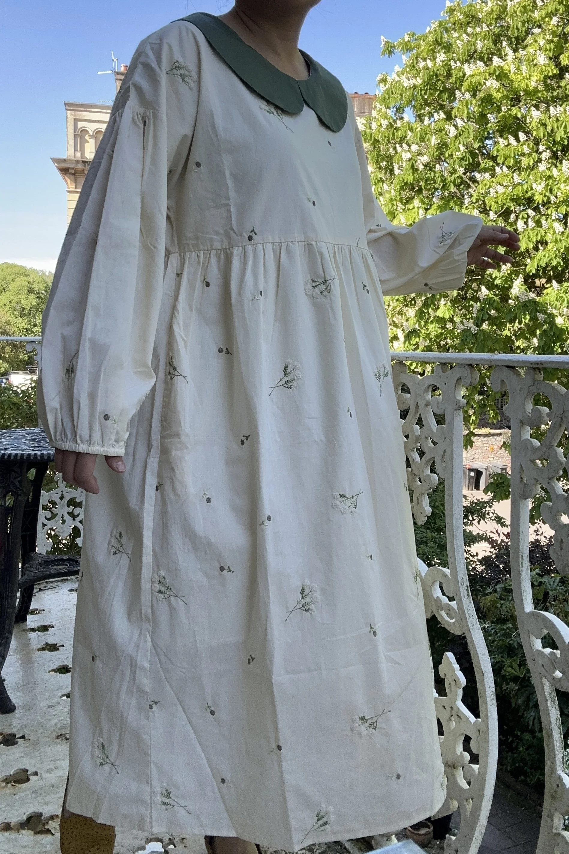 woman wearing Peter Pan collar maxi summer dress lace flowers embroidery standing on a balcony
