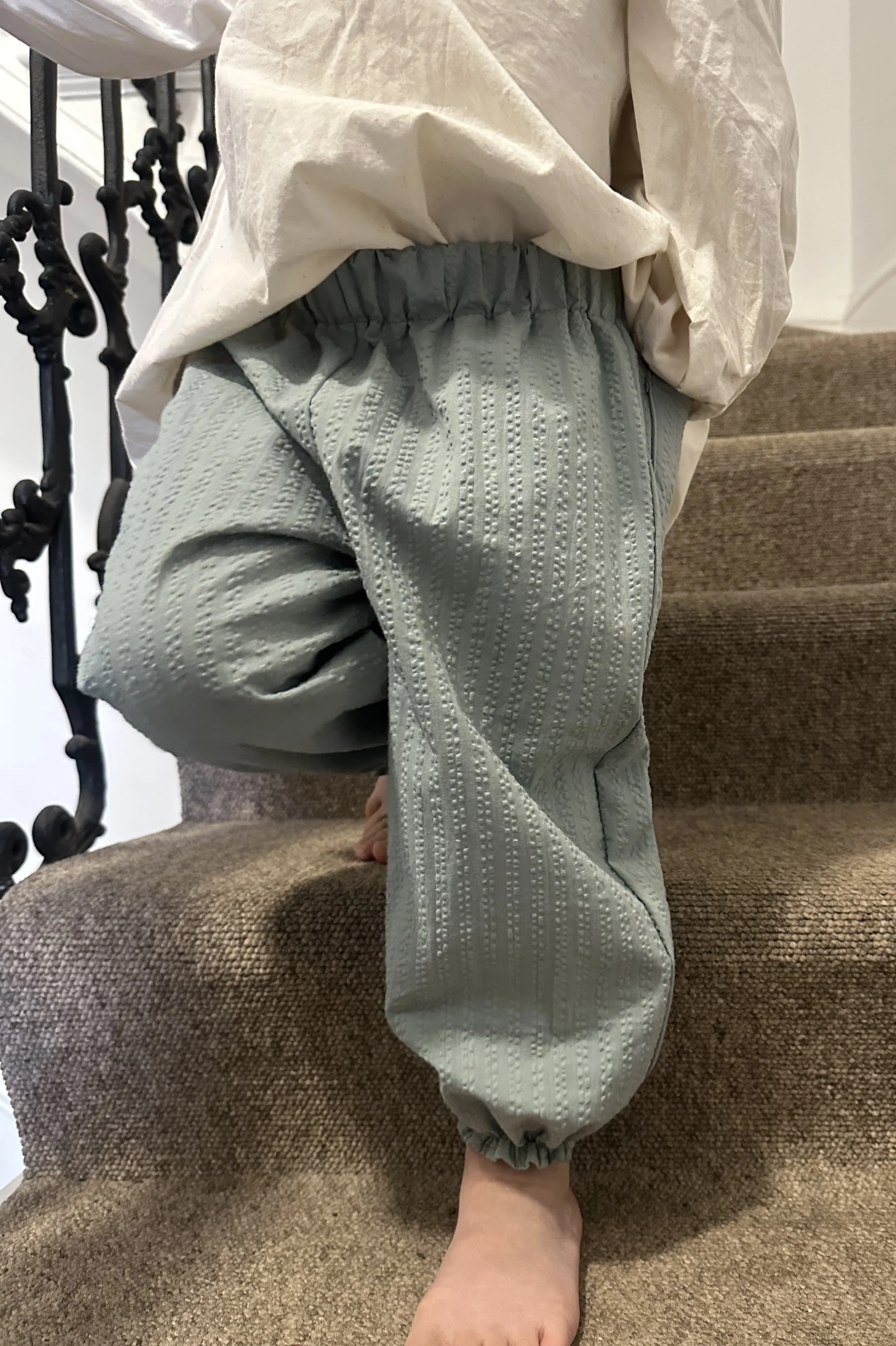 close up child wearing organic cotton seersucker barrel trousers duck egg colour, paired with cream white blouse with large frill collar, pearl hairband
