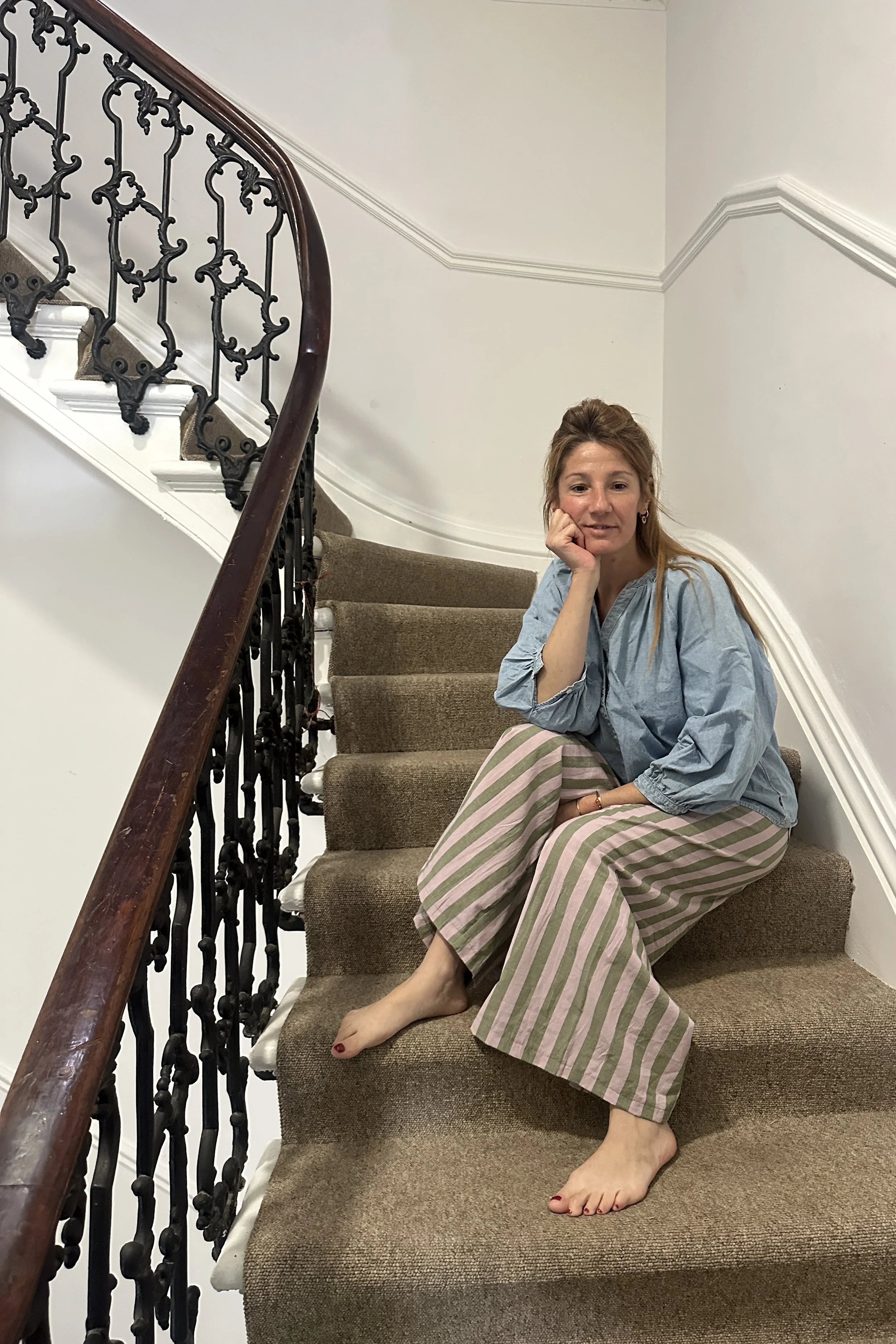 mum wearing organic cotton linen wide leg trousers stripes olive green and lilac, with denim light blue blouse sitting on the stairs