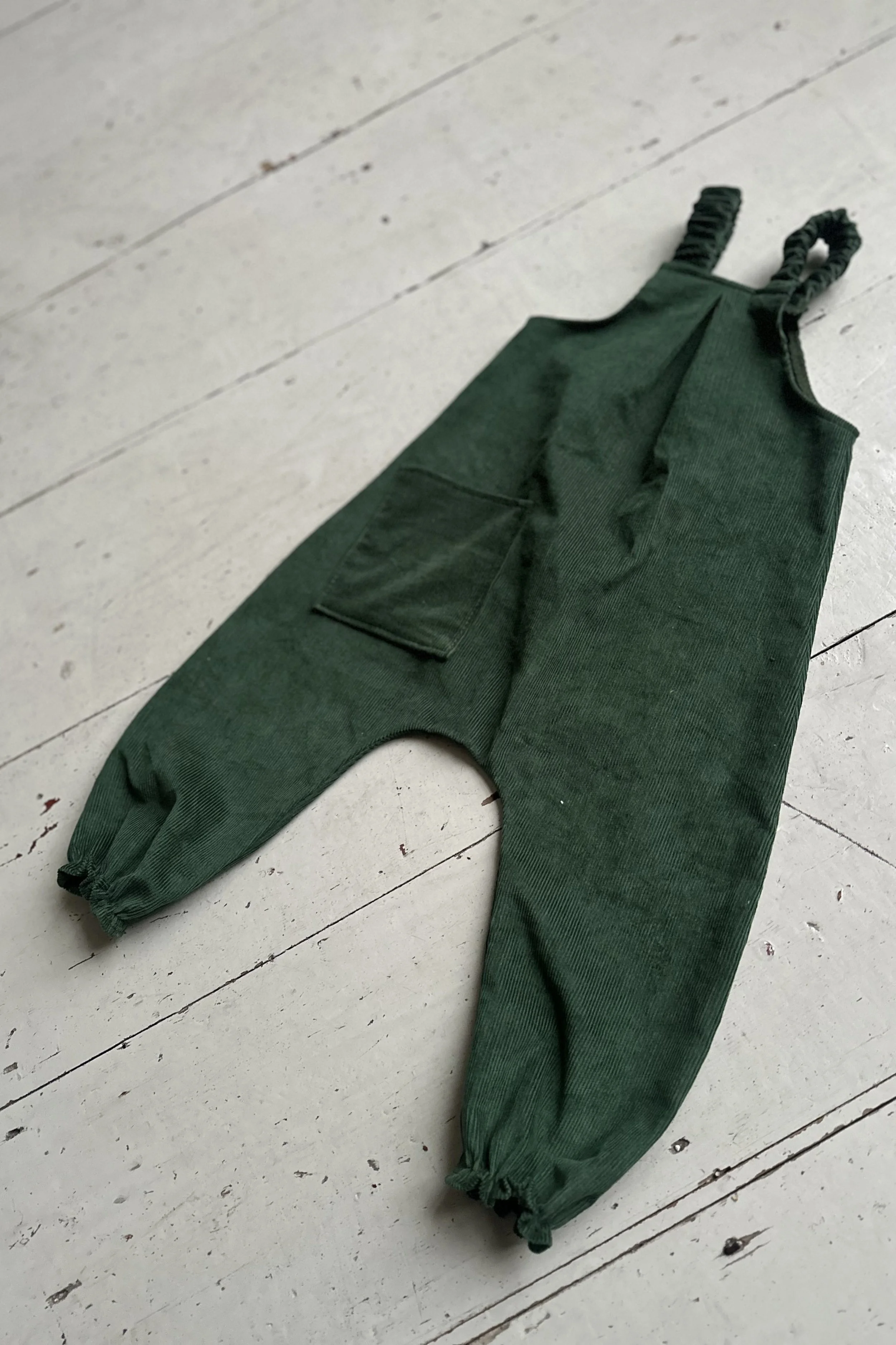 flatlay back of dark green organic needlecord pullover dungarees