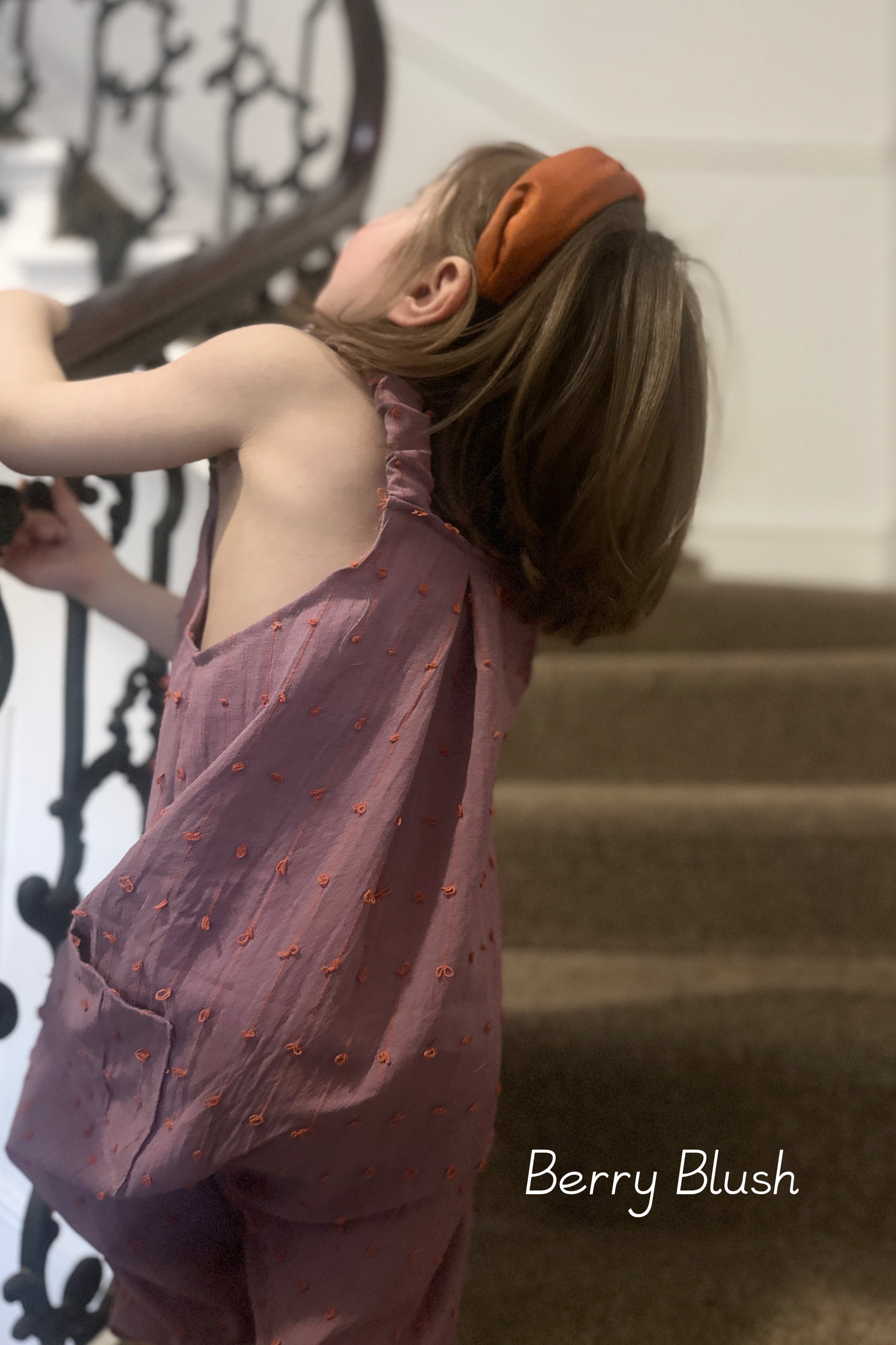 close up back and side of child wearing organic cotton loops dungarees berry blush colour standing on staircase