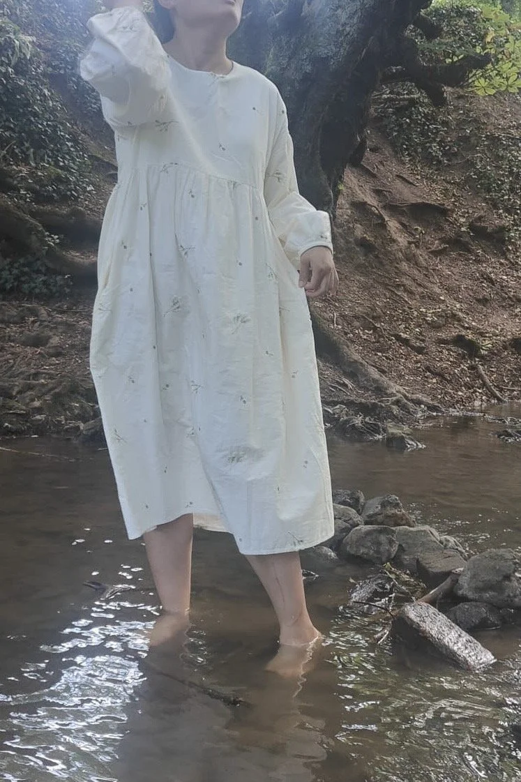 woman wearing while lace flowers embroidered maxi dress walking in a stream in wood