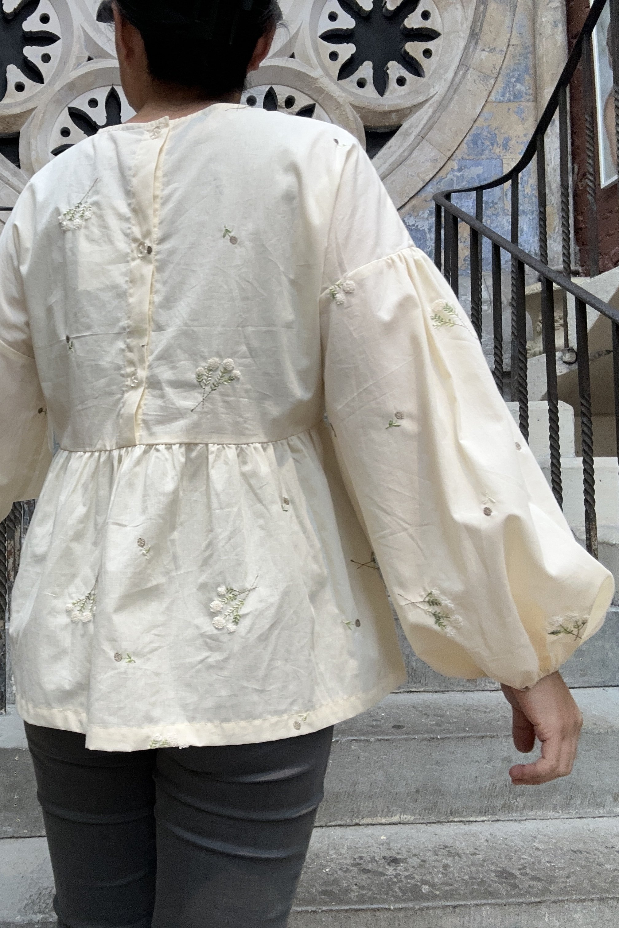 back view of Adult wearing embroidered lace flower Top, Featuring a relaxed fit, balloon sleeves, a statement line of buttons at the back