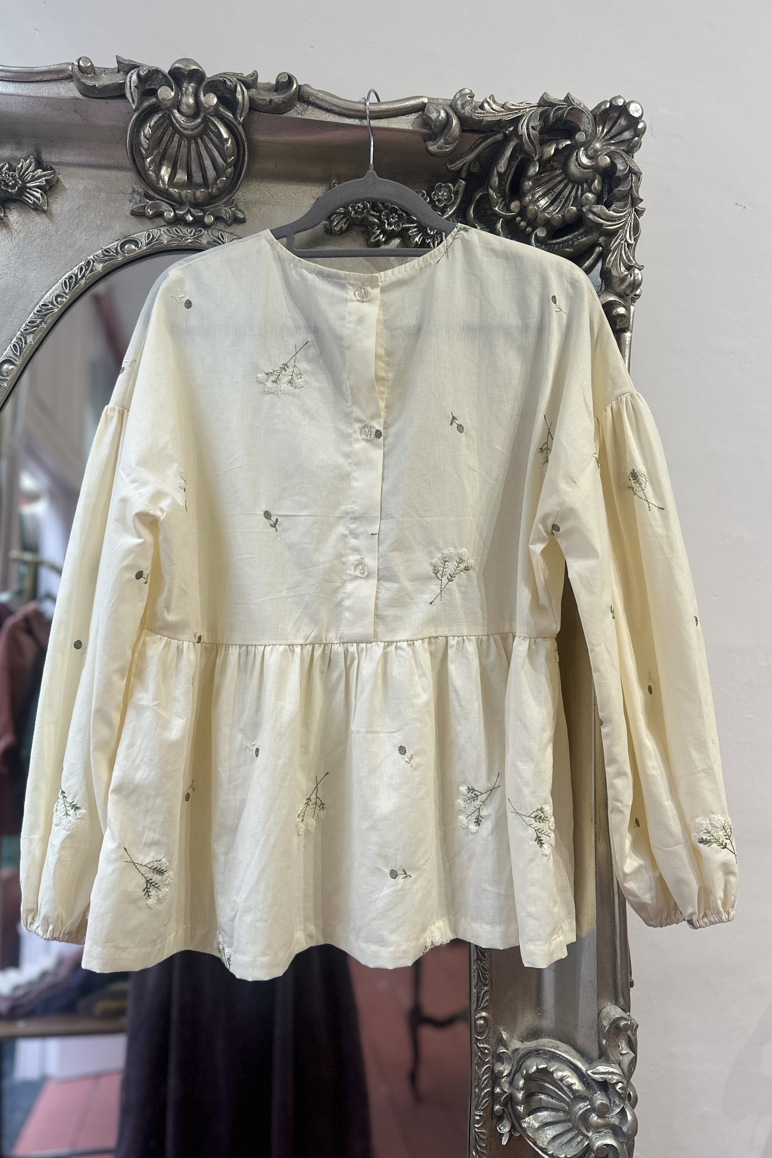 back view of hanging adult embroidered lace flower Top, Featuring a relaxed fit, balloon sleeves, a statement line of buttons at the back