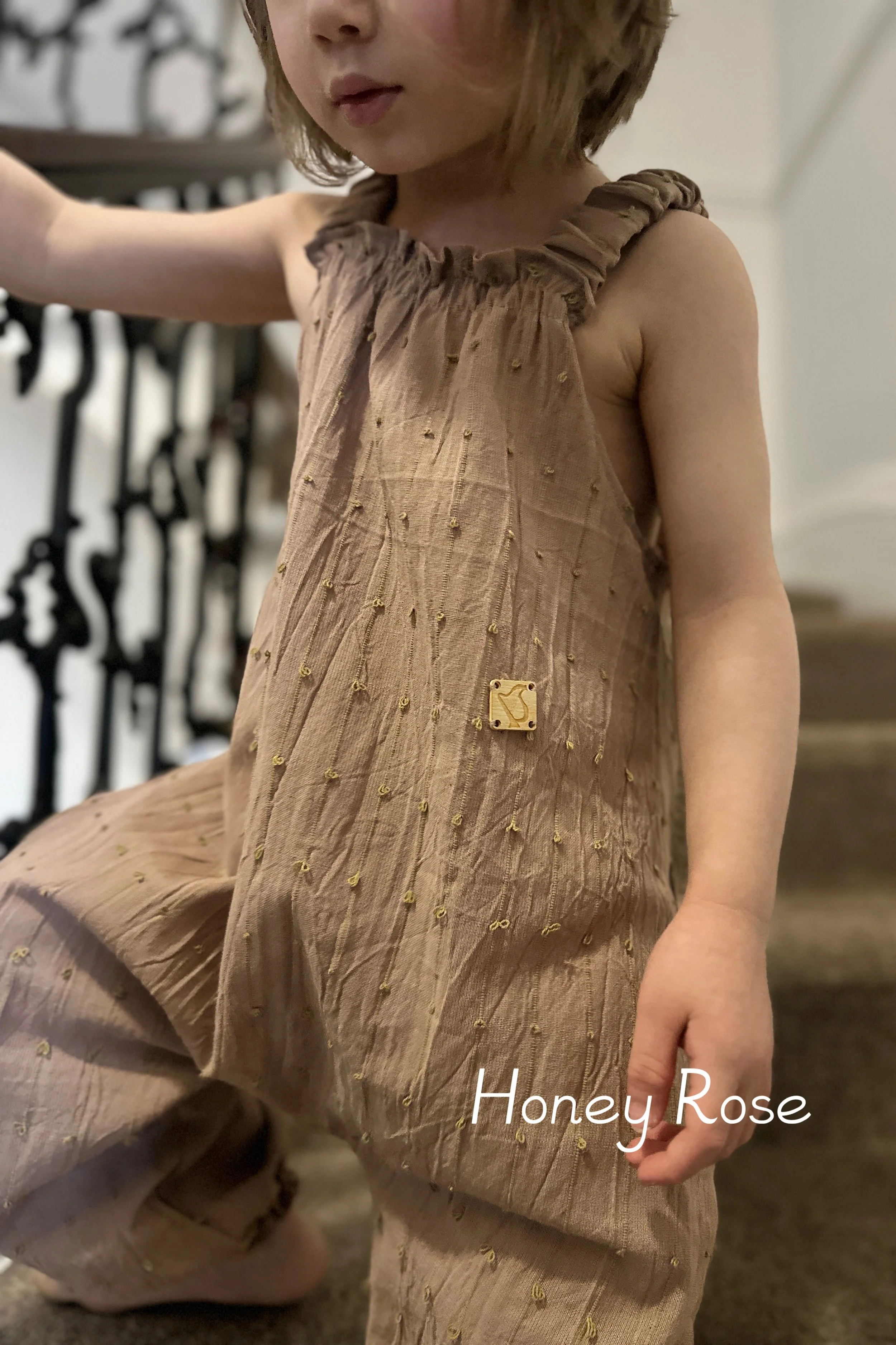 child wearing organic cotton loops dungarees honey rose colour standing on staircase