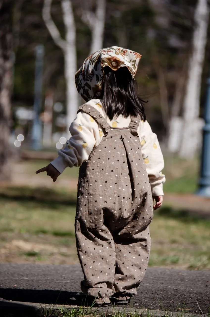 back view of. child wearing organic cotton speckled cocoa dungarees, floral handkerchief,