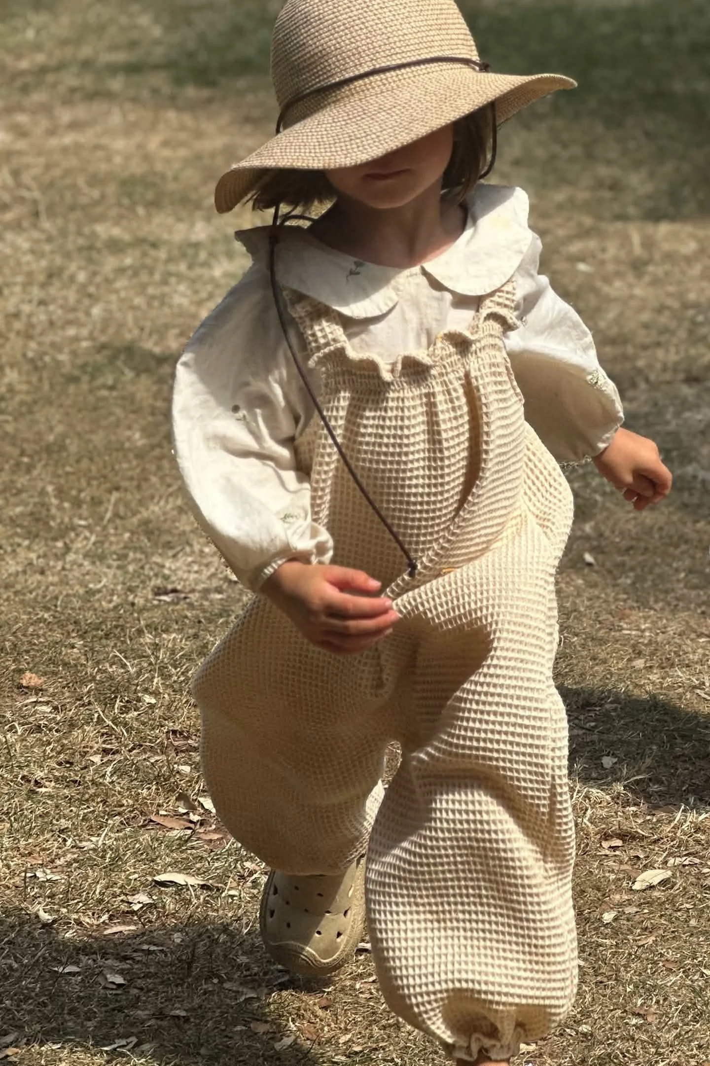 child wearing organic cotton waffle natural white dungarees layered with white blouse, sun hat