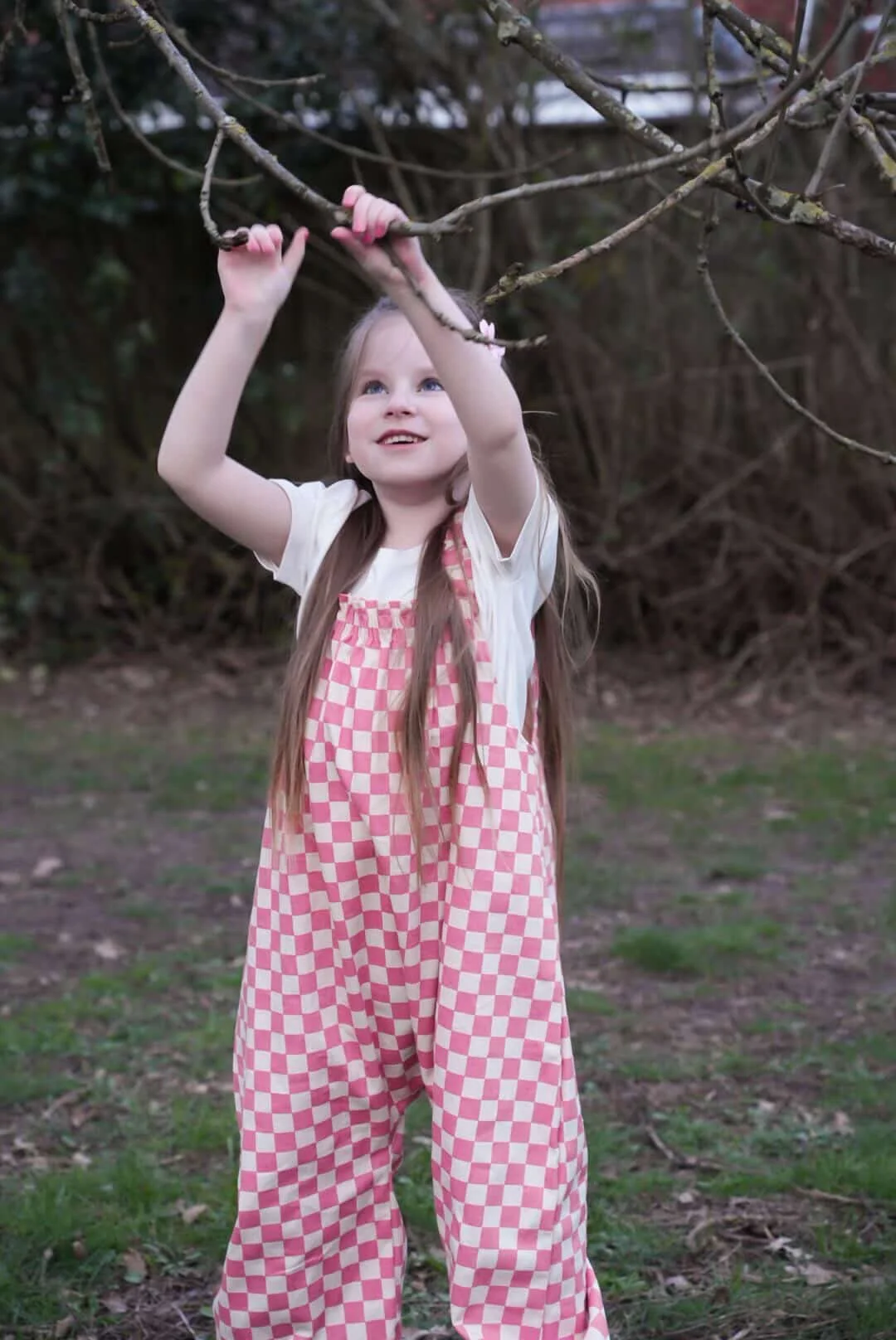 girl wearing organic cotton checkerboard dungarees in pink