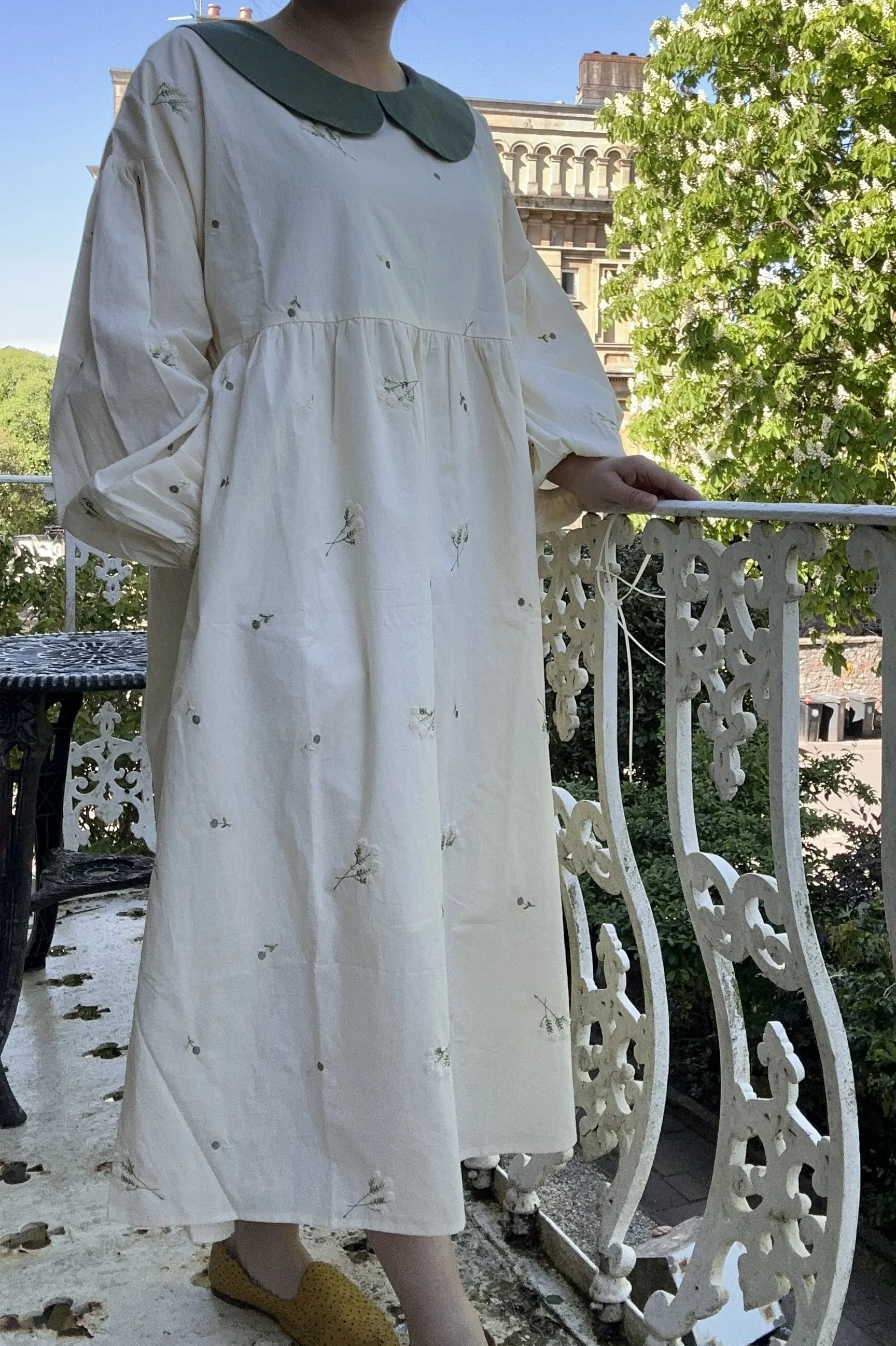 woman wearing Peter Pan collar maxi summer dress lace flowers embroidery standing on a balcony