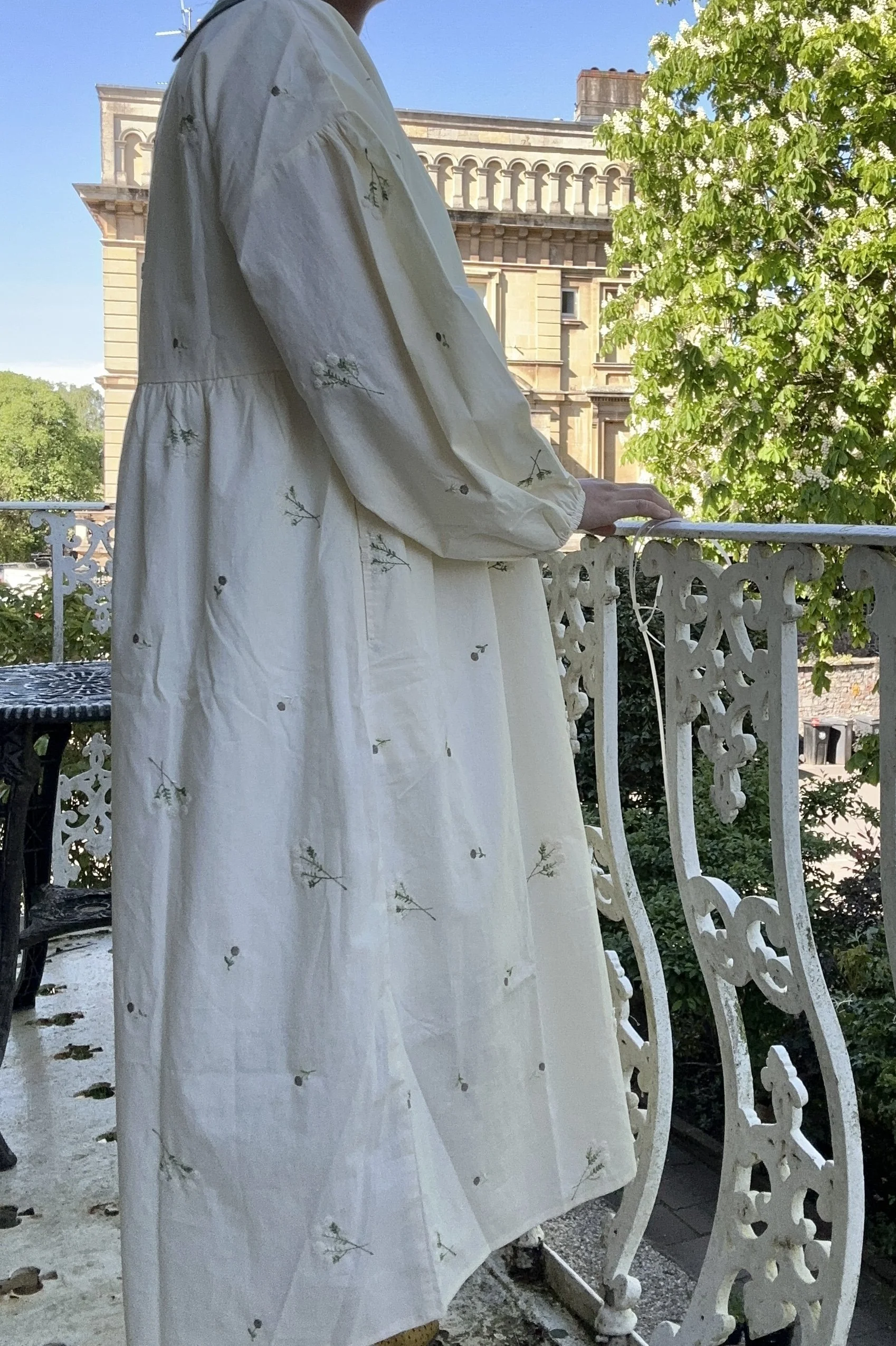 side view of woman wearing Peter Pan collar maxi summer dress lace flowers embroidery standing on a balcony