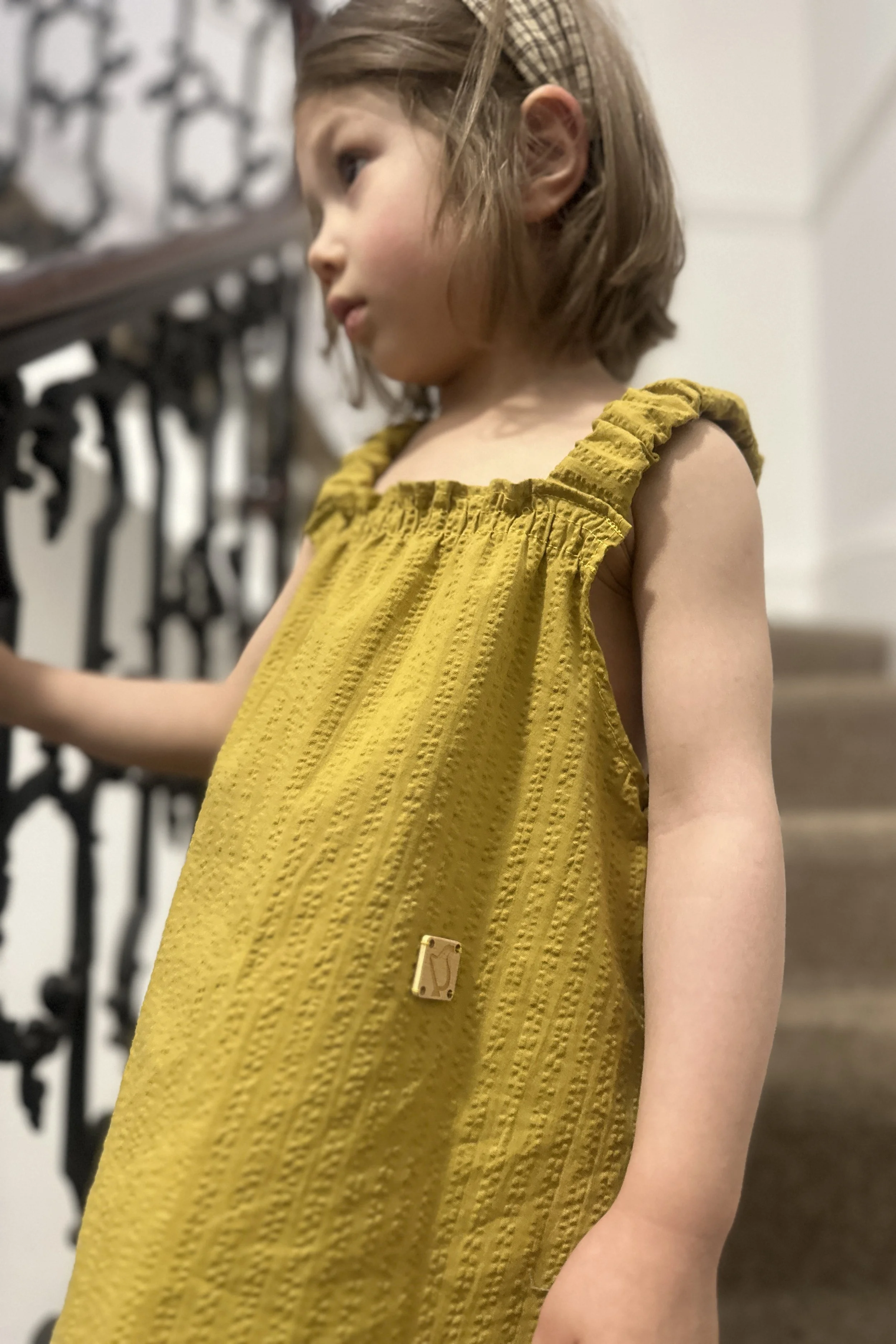 front of child wearing organic cotton seersucker stripe mustard dress standing on staircase