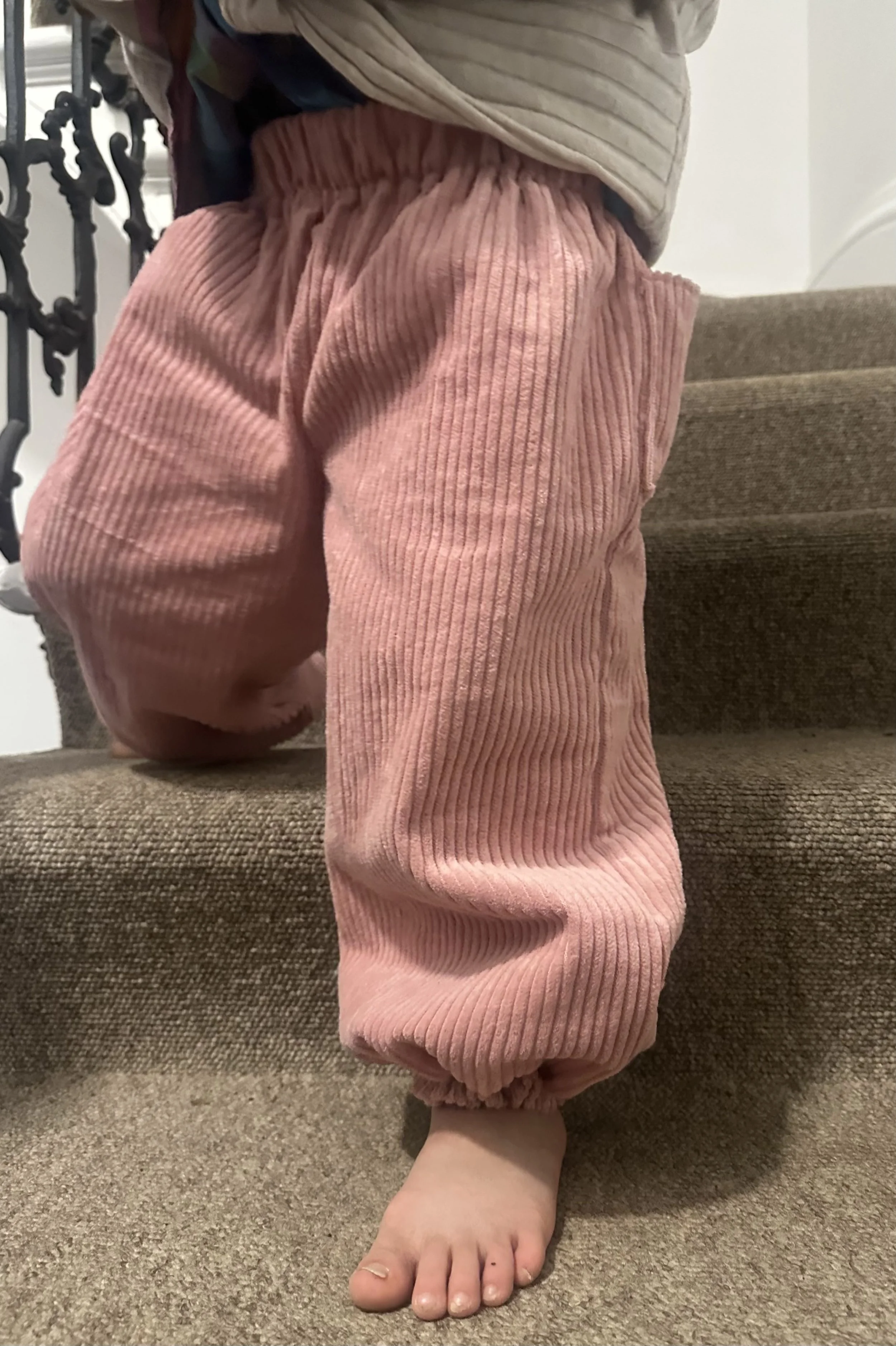 close up child wearing organic cotton corduroy pink trousers barrel shape baggy fit oversized elastic hem, highlighting elastic waistband and elastic hem