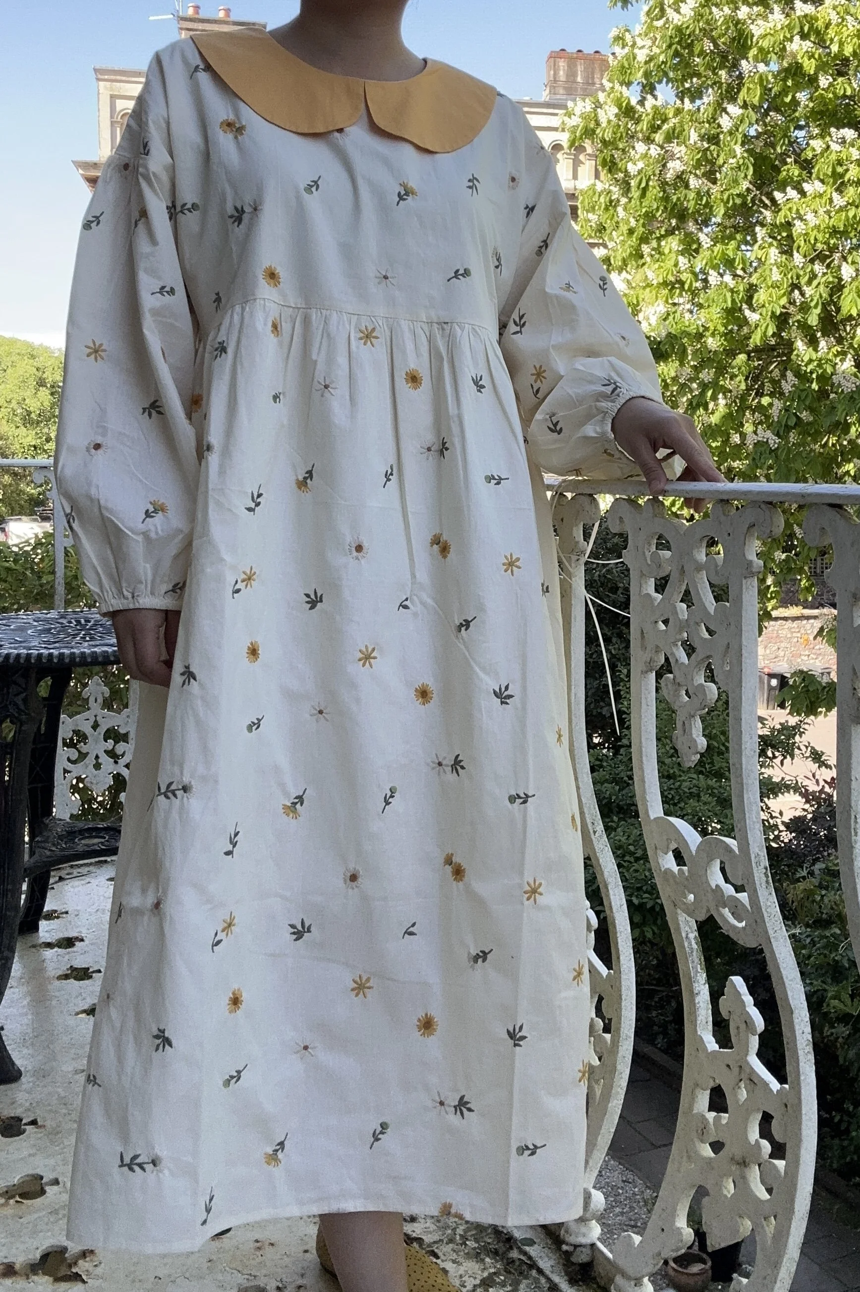 woman wearing Peter Pan collar maxi summer dress dandelion embroidery standing on a balcony