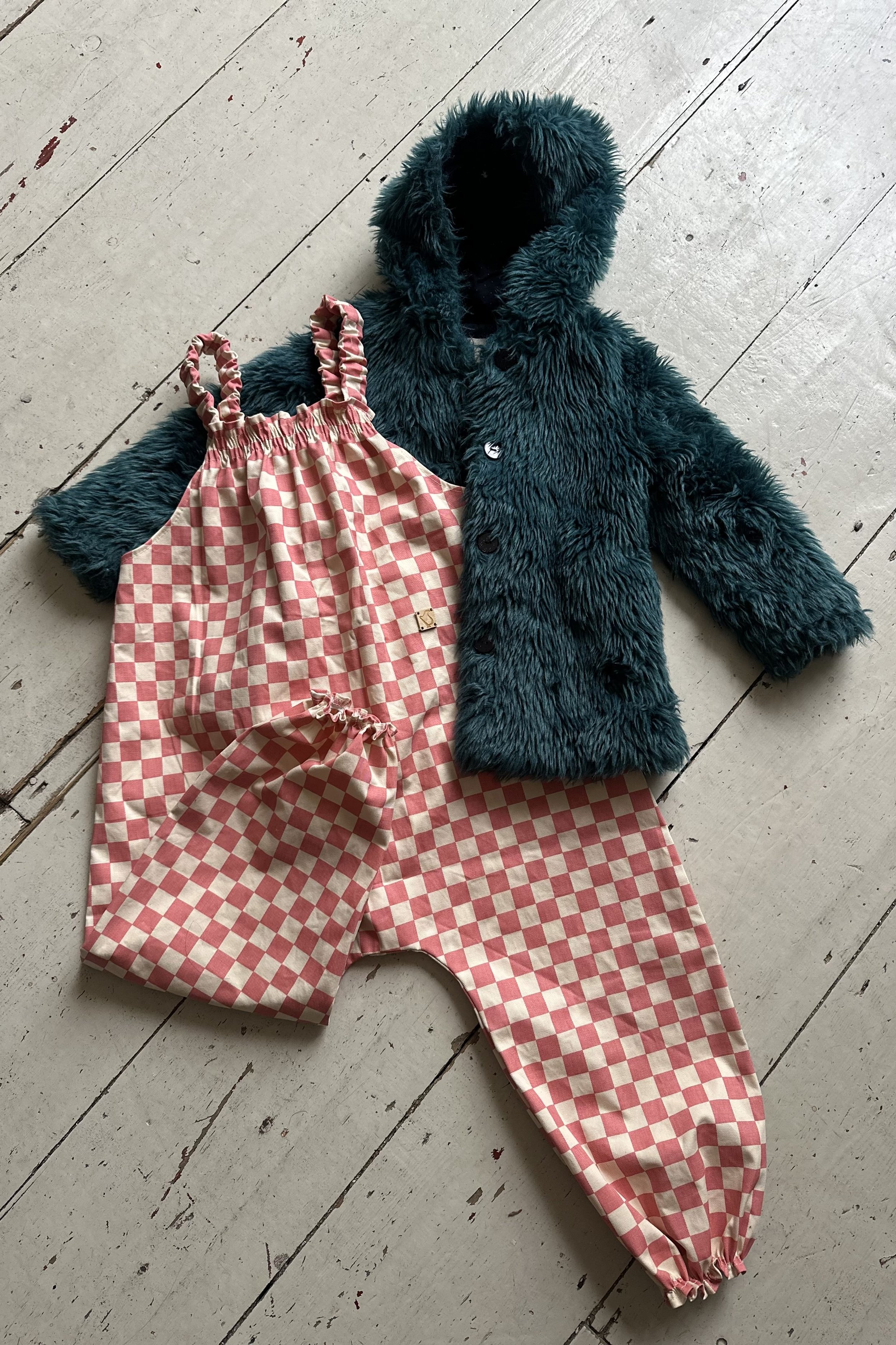 flatlay child organic cotton pullover dungarees checkerboard pink, styled with a dark green faux fur hoodied coat