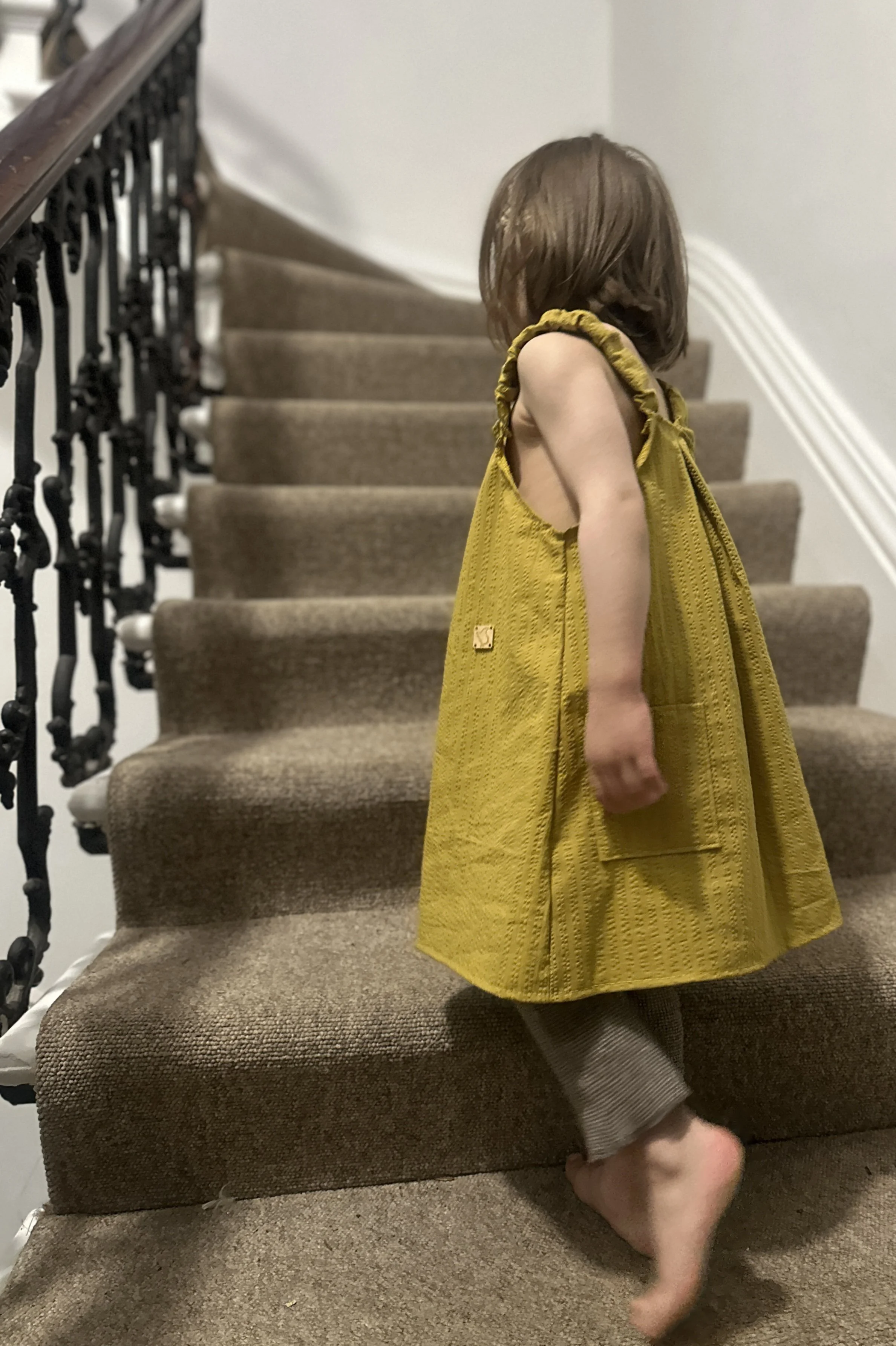 side of child wearing organic cotton seersucker stripe mustard dress standing on staircase