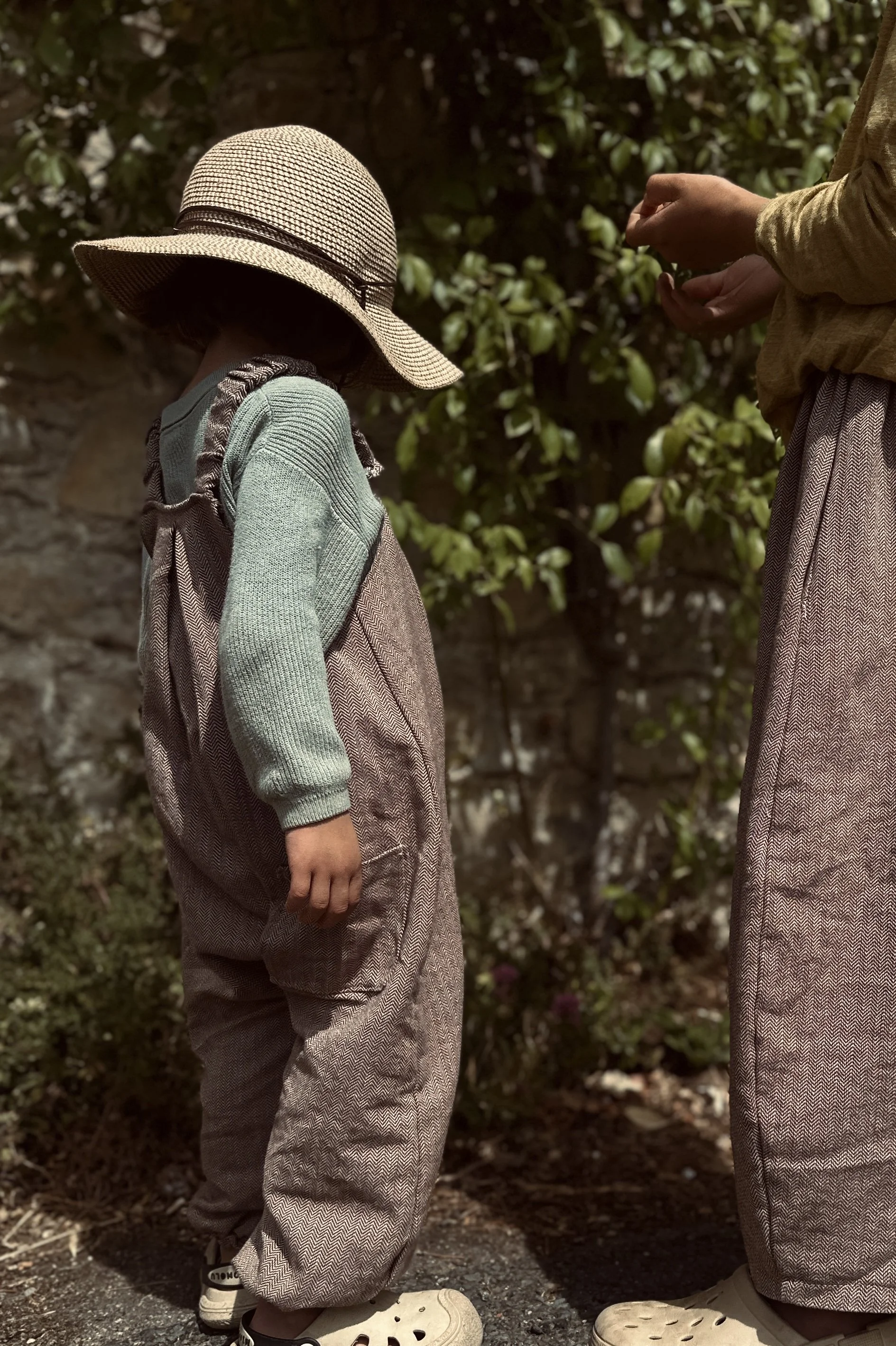 side view of child wearing organic cotton herringbone brown dungarees layered with sage green jumper