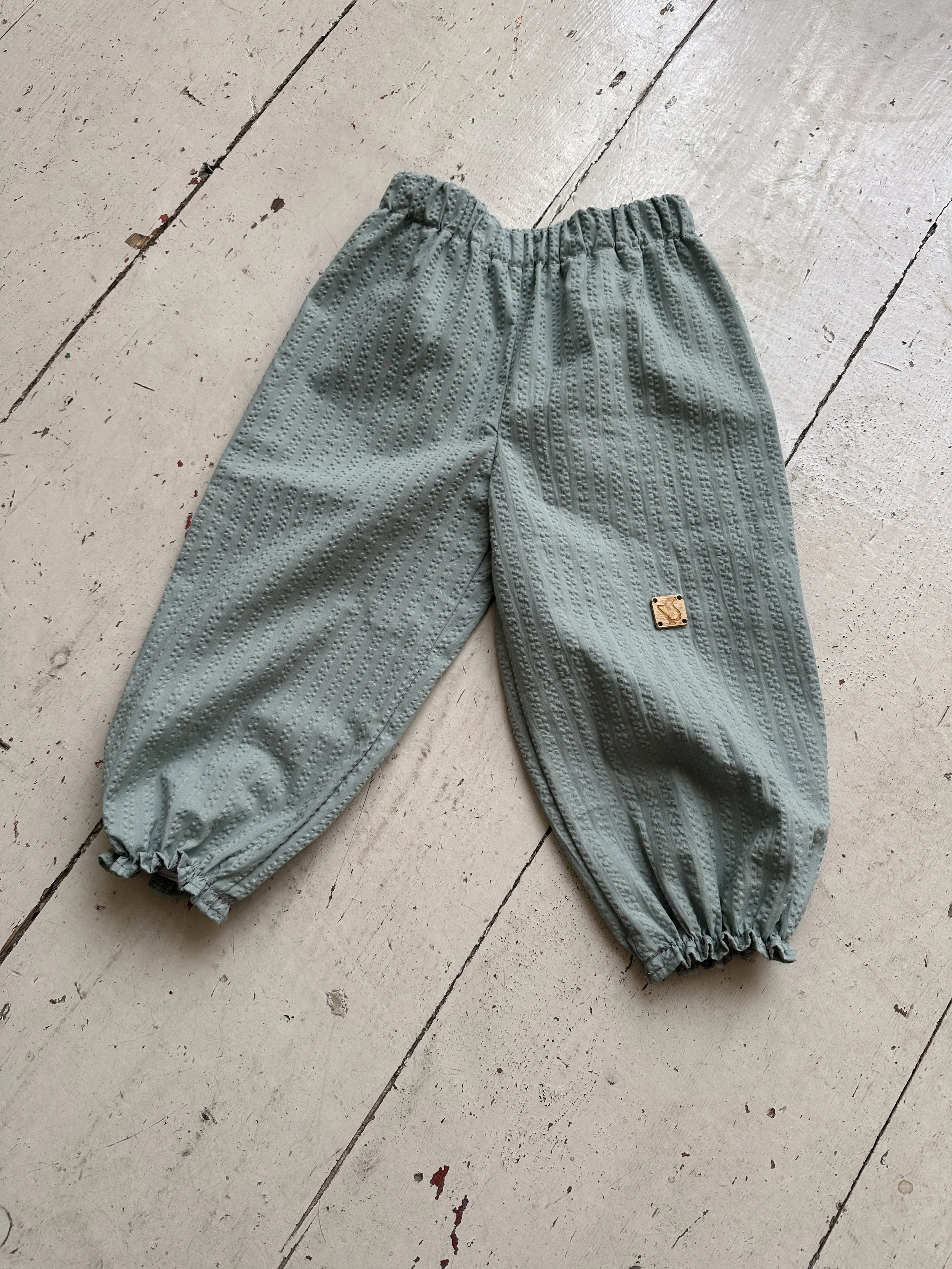 flat lay of organic cotton seersucker barrel trousers duck egg colour