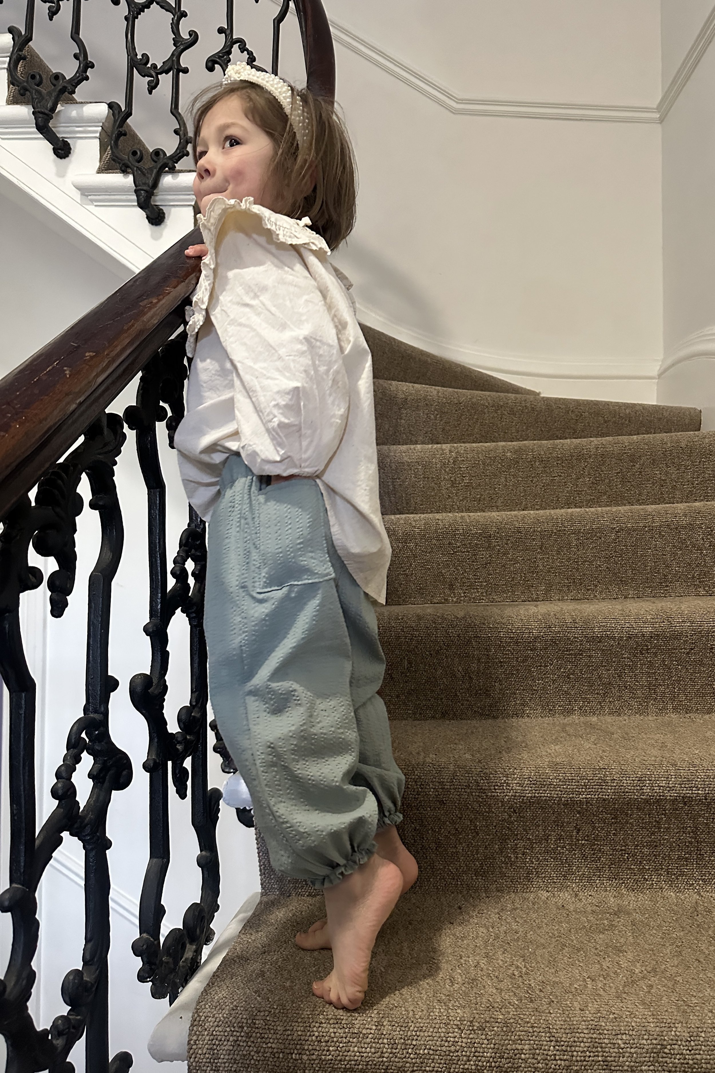 side view of child wearing organic cotton seersucker barrel trousers duck egg colour, paired with cream white blouse with large frill collar, pearl hairband