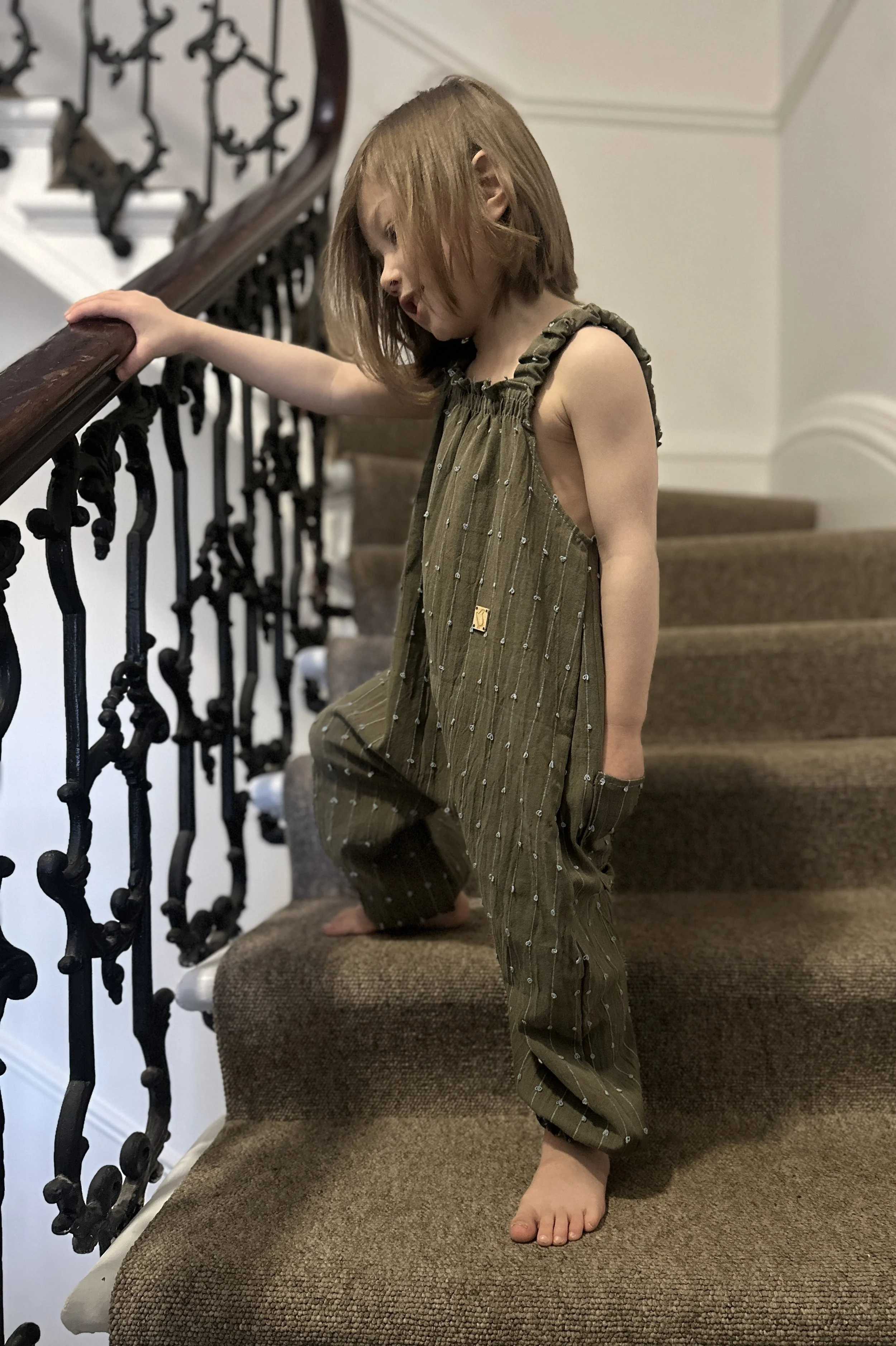 child wearing organic cotton loops dungarees turquoise sage colour standing on staircase