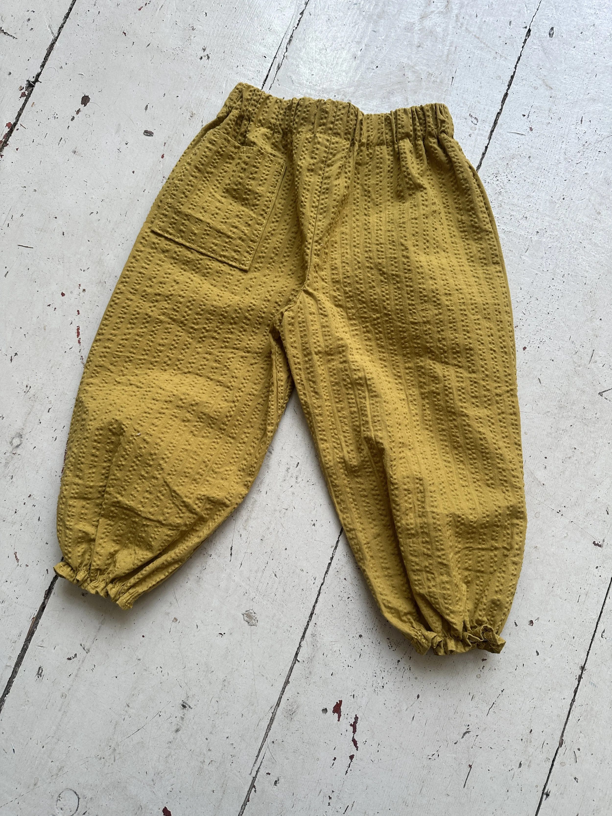 flat lay back of organic cotton seersucker barrel trousers mustard colour