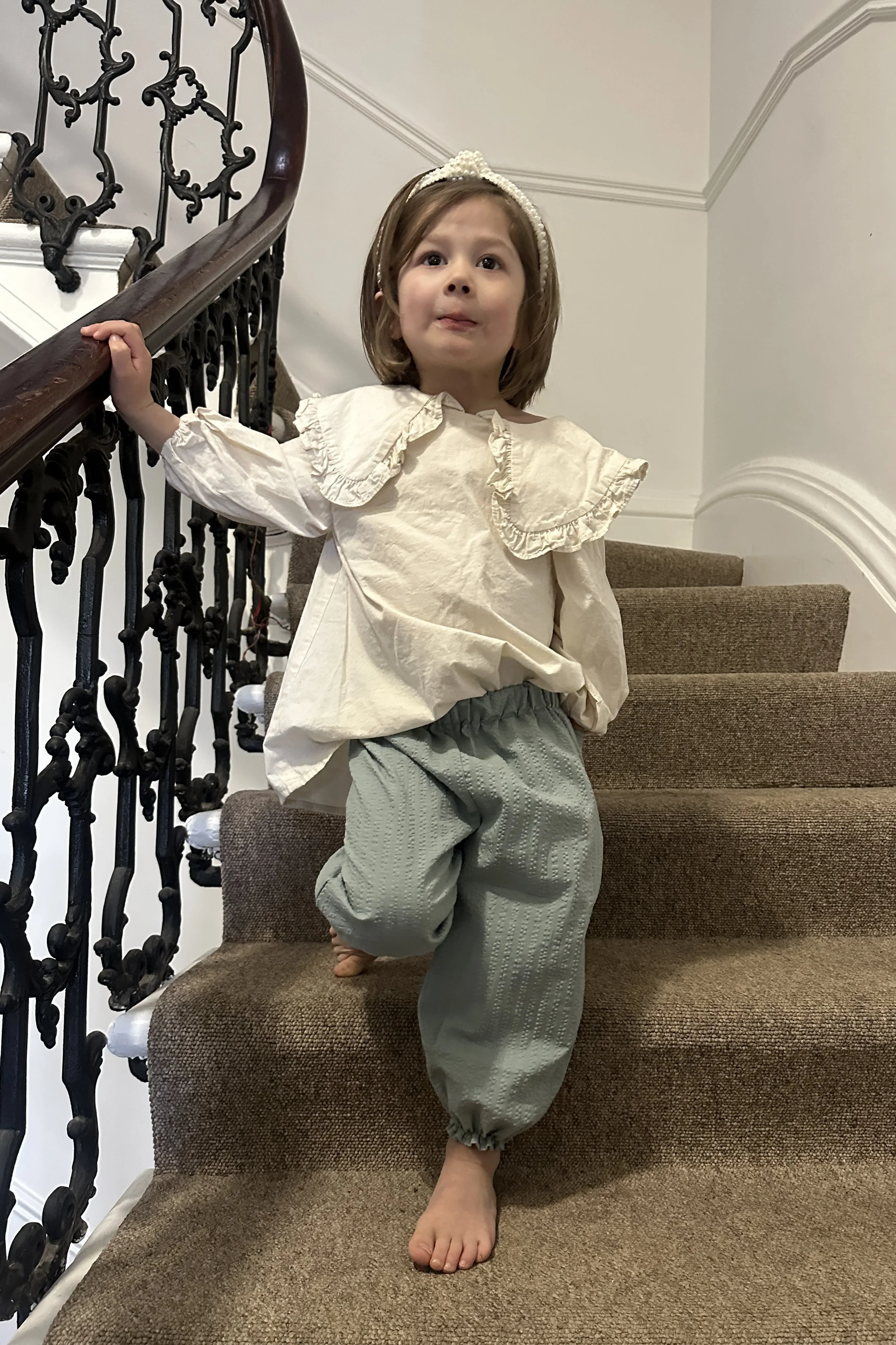 child wearing organic cotton seersucker barrel trousers duck egg colour, paired with cream white blouse with large frill collar, pearl hairband